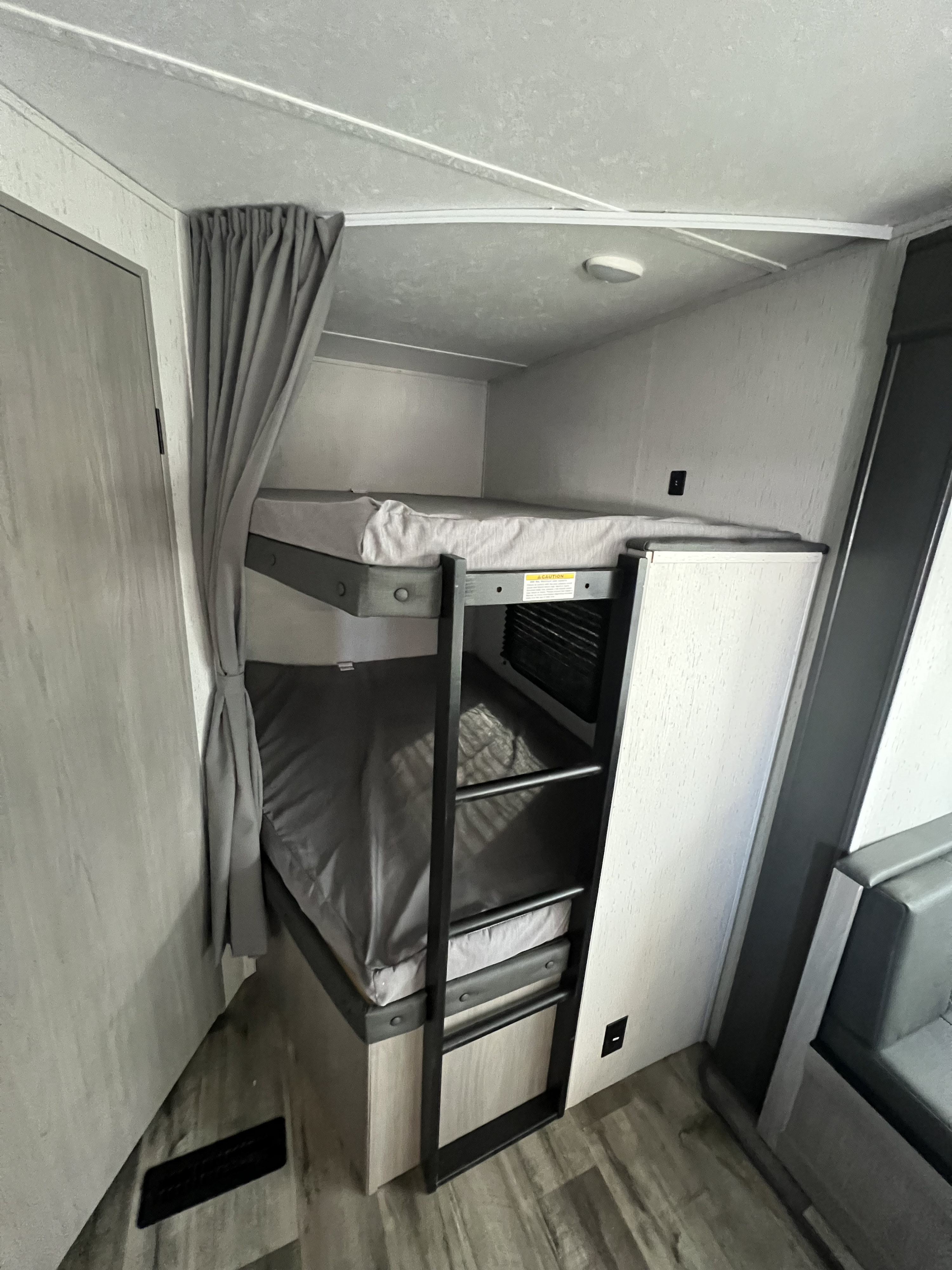 RV rental bunk beds feature grey bedding, a sturdy ladder, and a privacy curtain, providing a compact, cozy sleeping area.. Coleman Lantern 263BHWE 263BHWE 2024