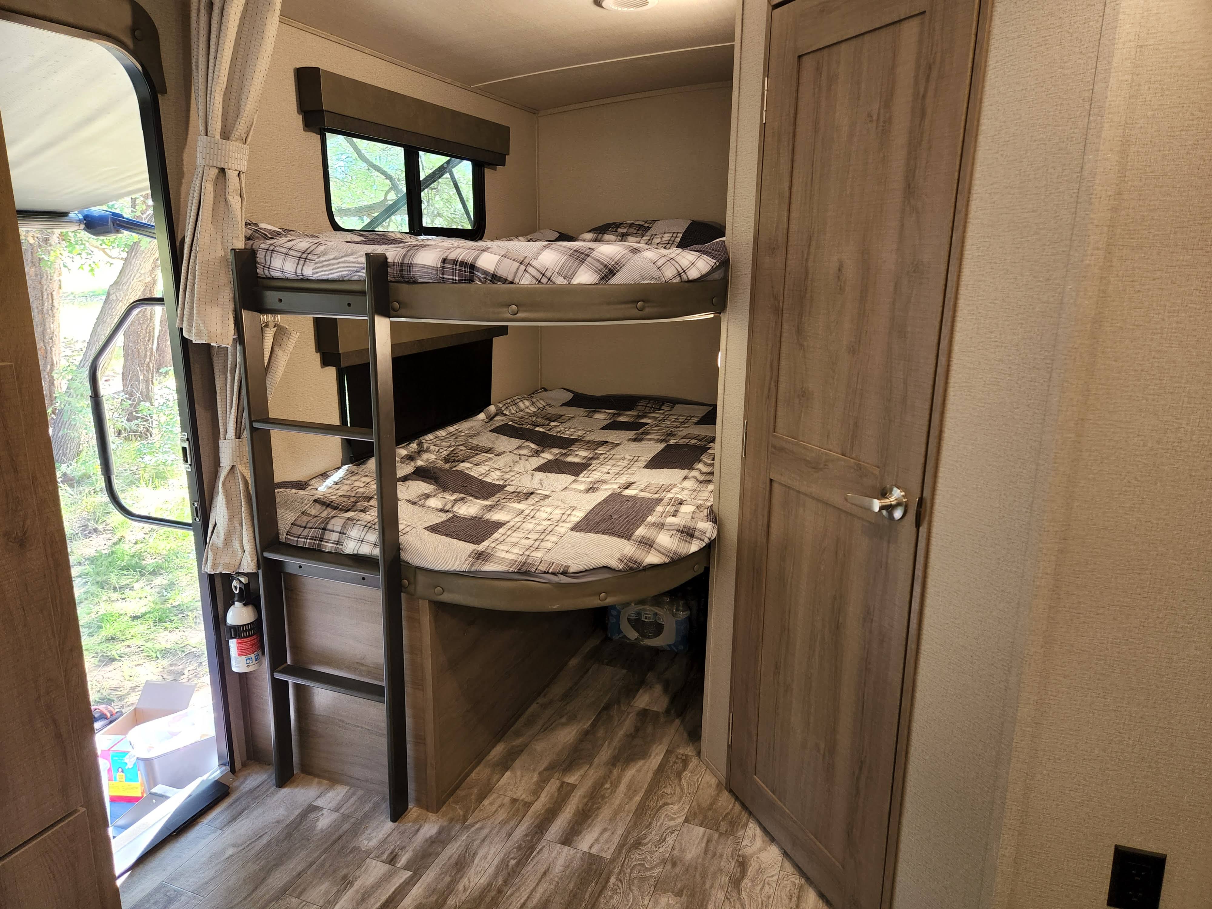 RV rental interior featuring bunk beds with plaid bedding, a wooden door, and an open entryway revealing outdoor trees.. Grand Design Imagine 2021
