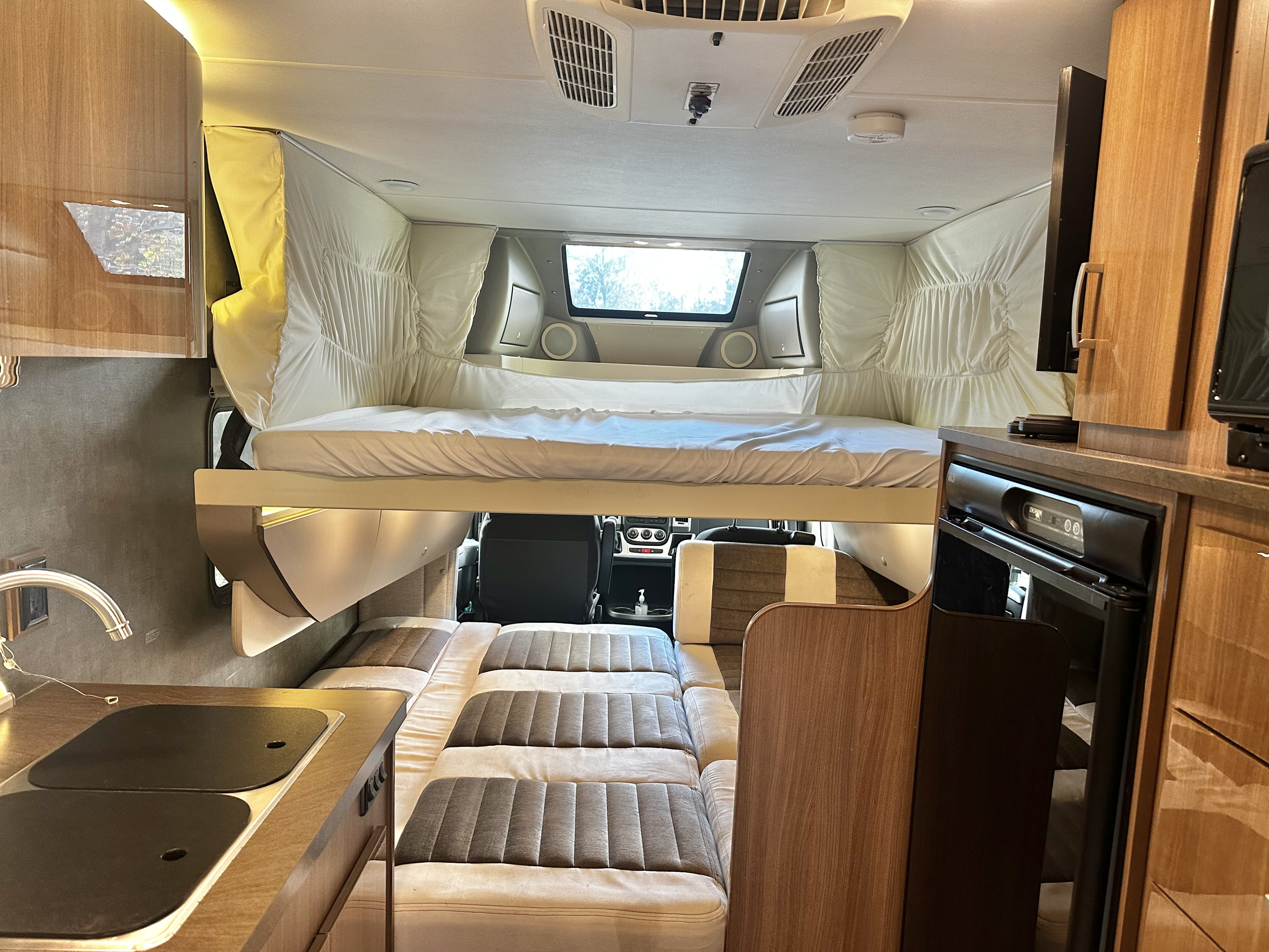 Interior of an RV rental showing an over-cab bed, convertible dinette/lower bed, and full kitchen.. Winnebago Trend 2015