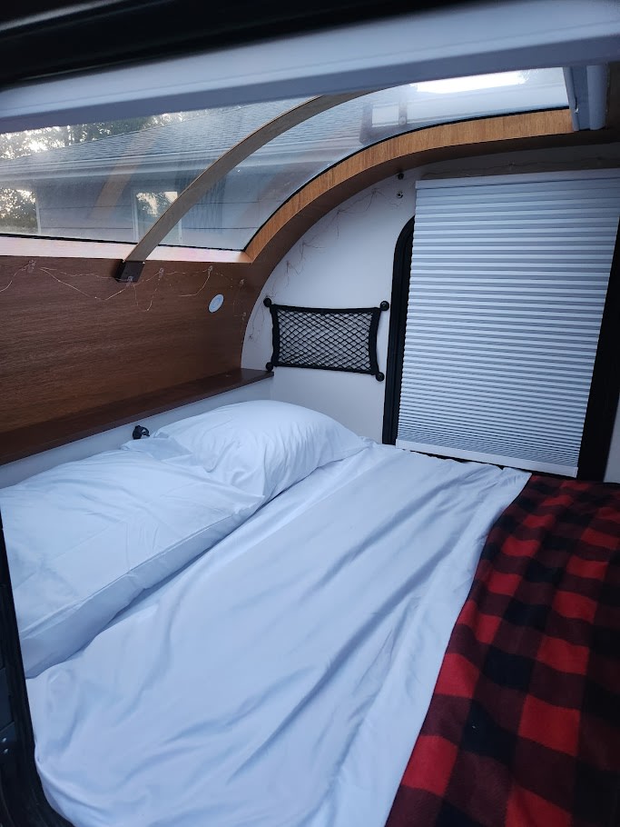Cozy RV rental interior with a comfortable bed, white sheets, and a red plaid blanket, ready for your adventure.. Driftwood Custom 2021