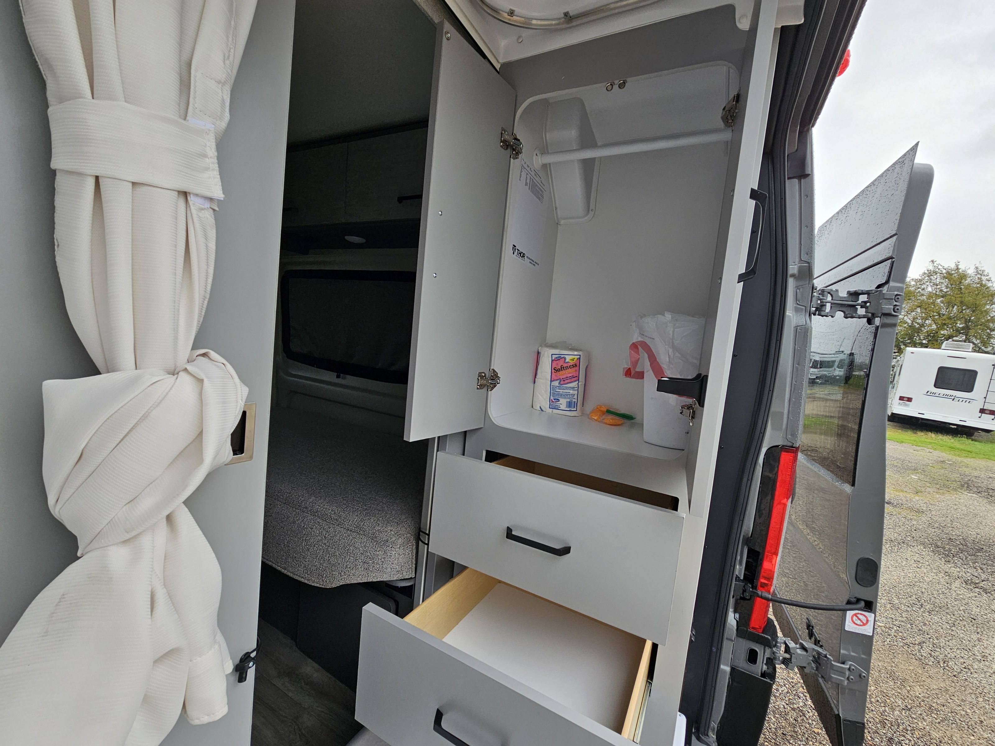 RV rental's functional interior: open storage cabinet with supplies, pull-out drawers, and open rear door view.. Thor Motor Coach Twist 2026