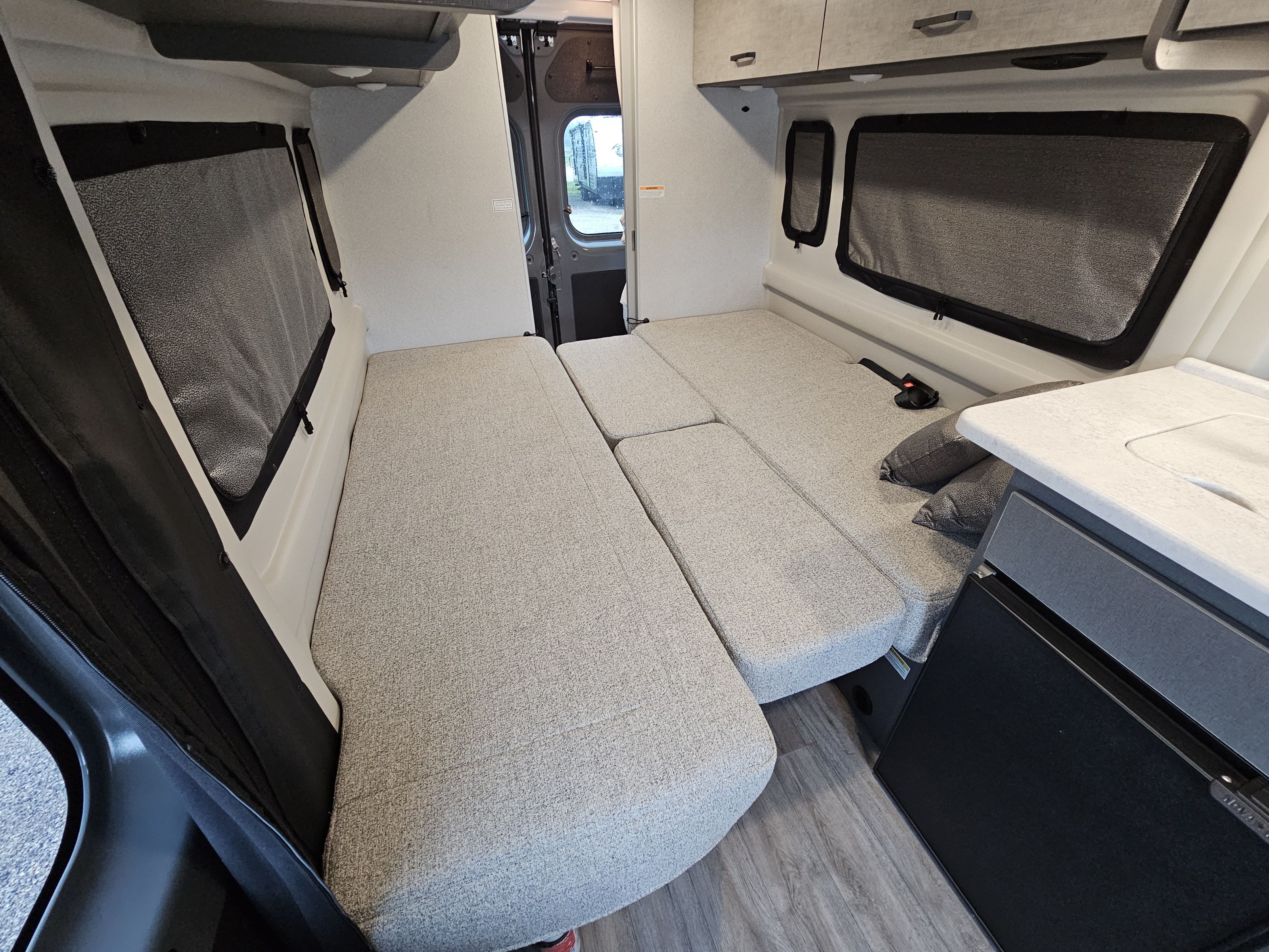Spacious RV rental interior featuring an L-shaped seating area converting to a bed, windows with shades, overhead cabinets, and a compact kitchen.. Thor Motor Coach Twist 2026
