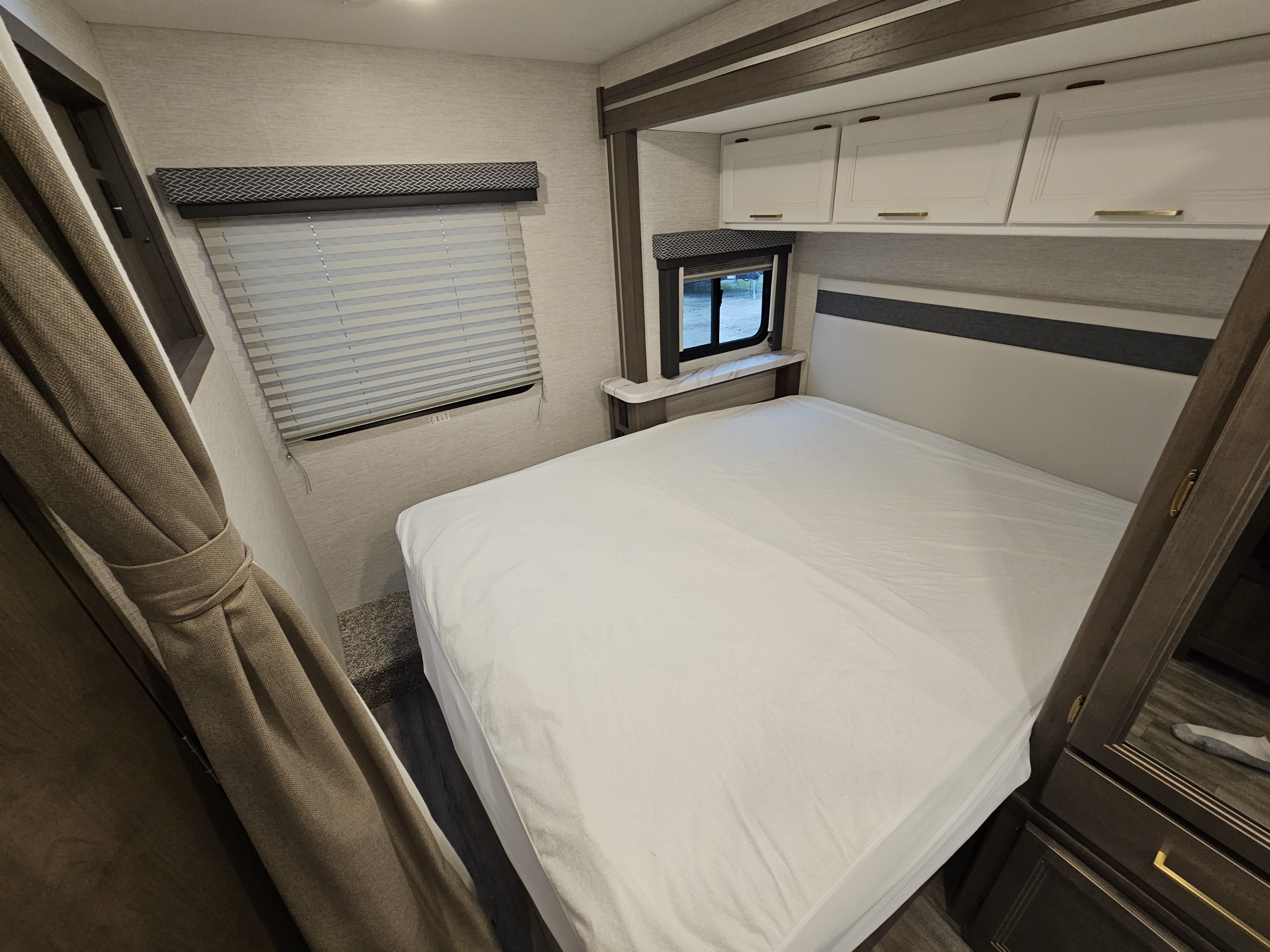 Clean RV rental bedroom with a white bed, overhead cabinets, and windows including one with an "EXIT" sign.. Thor Motor Coach Four Winds 2026