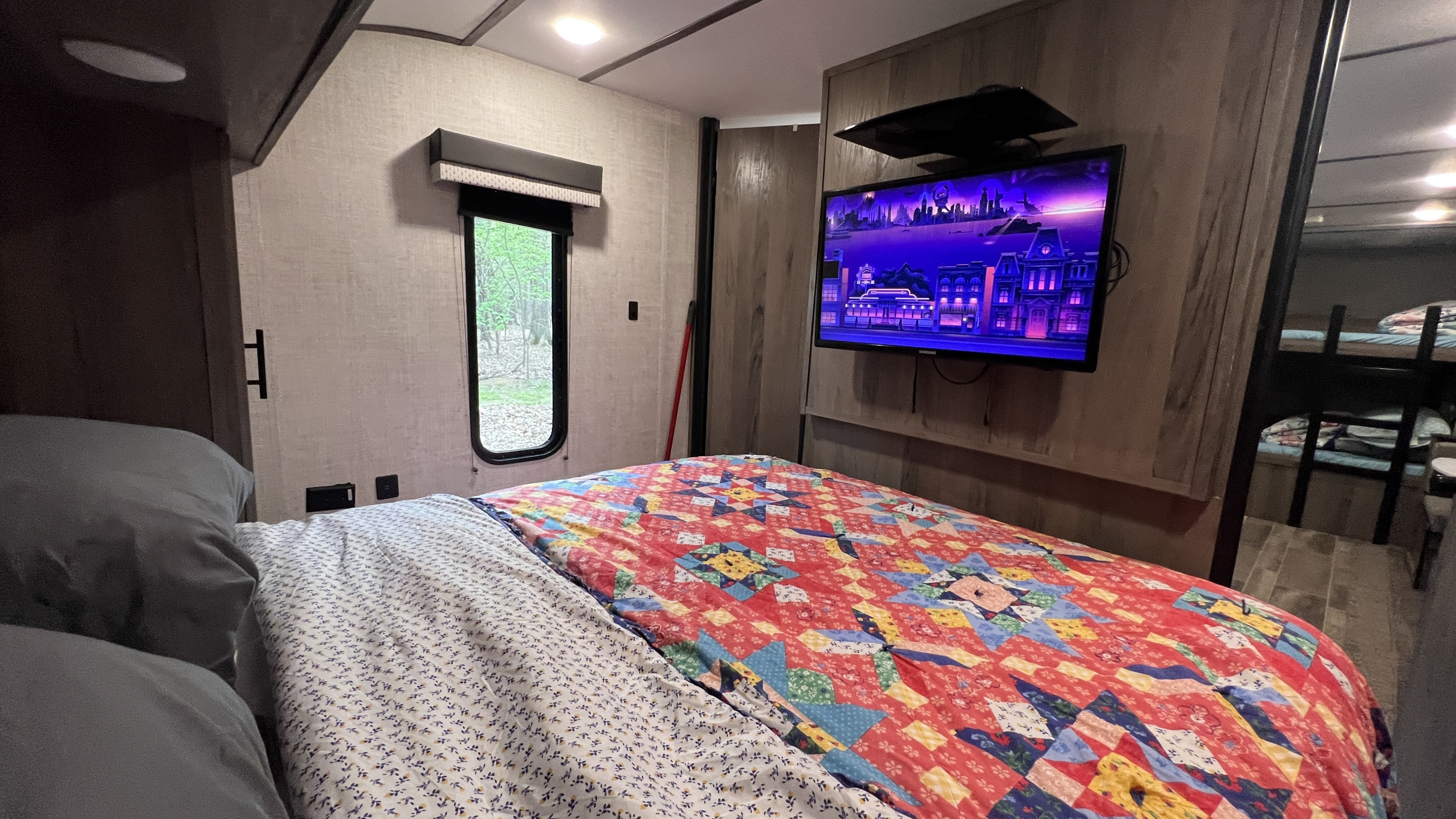 Cozy RV rental bedroom with a vibrant quilt, wall-mounted TV, window overlooking nature, and bunk beds.. Gulfstream Amerilite 2022