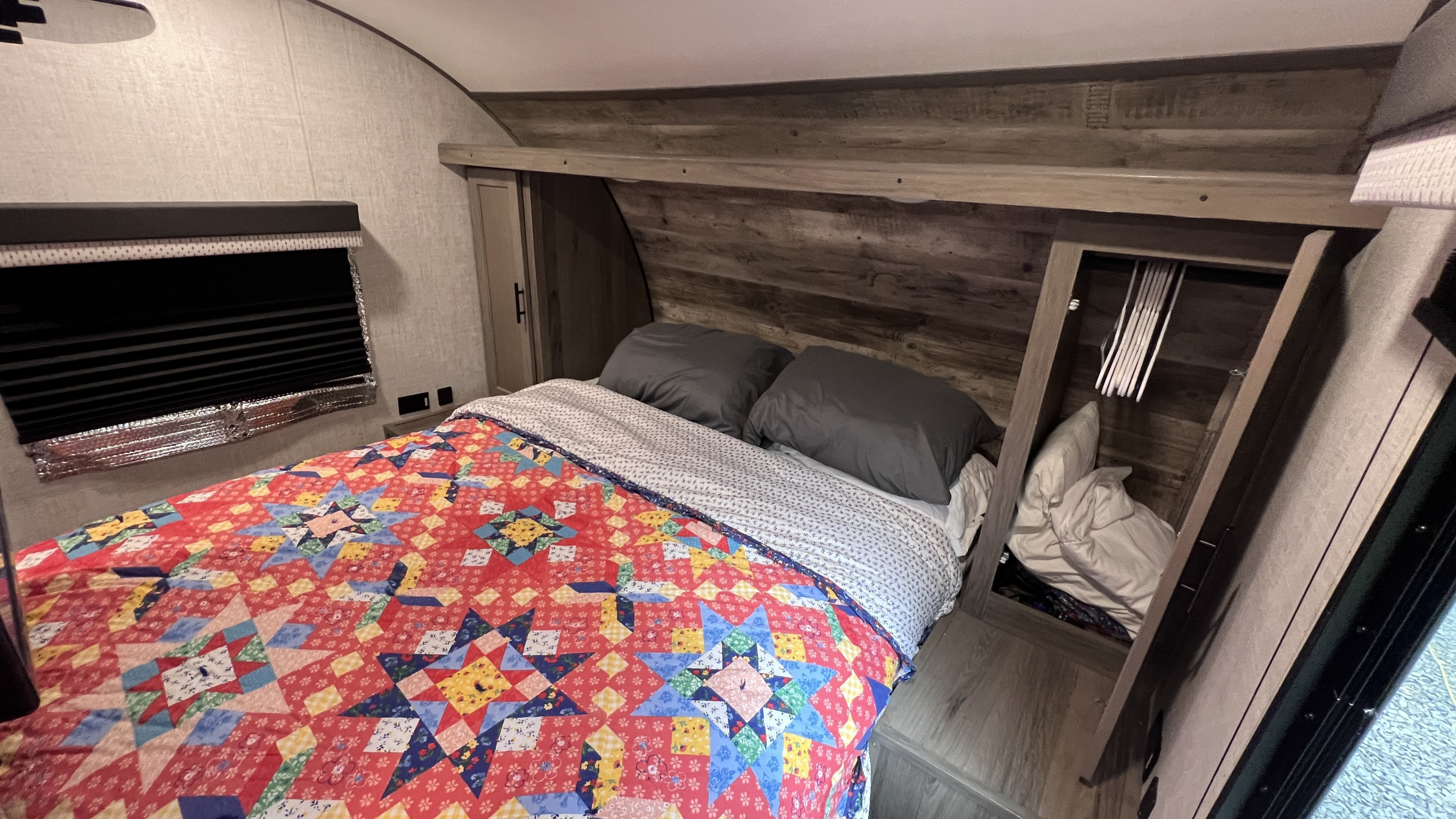 Cozy RV rental bedroom features a colorful quilt, window with blind, and convenient built-in storage.. Gulfstream Amerilite 2022