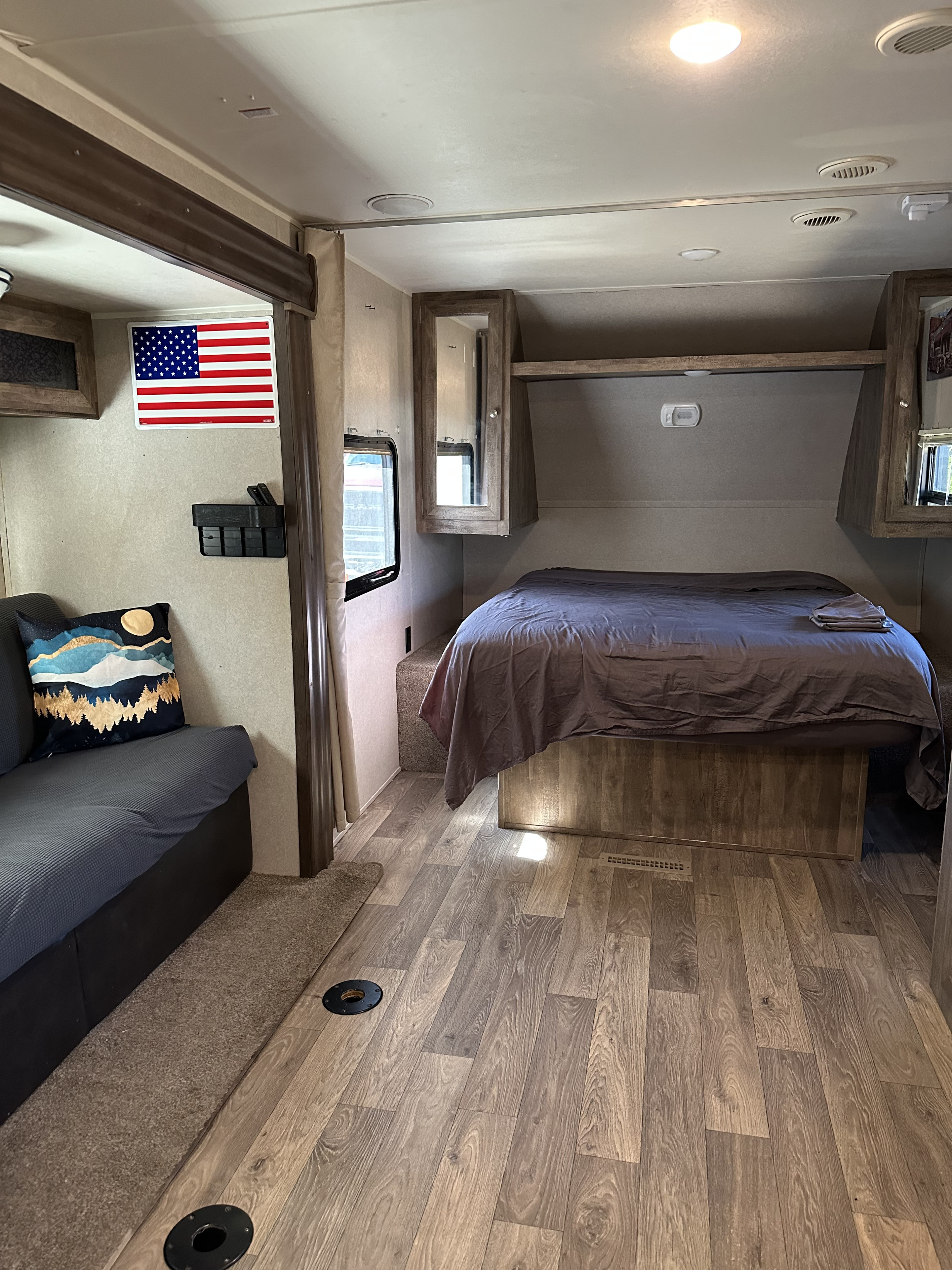 RV rental: Bright, clean travel trailer interior with a bed, sofa, wood-look floor, and American flag decor.. Palomino Real Lite 2018