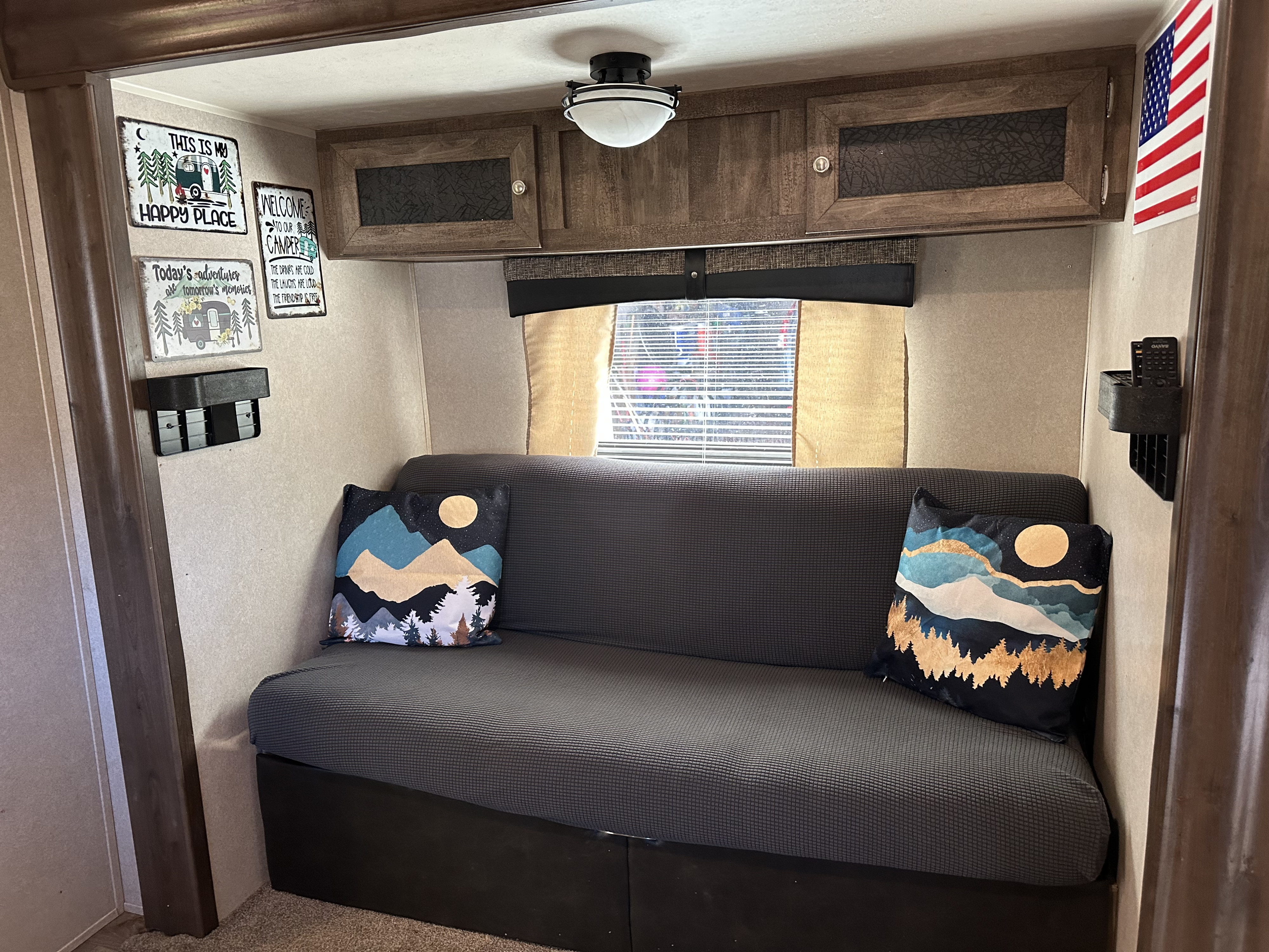 Cozy RV rental interior with a gray couch, mountain pillows, and camping signs, creating a welcoming camper living space.. Palomino Real Lite 2018
