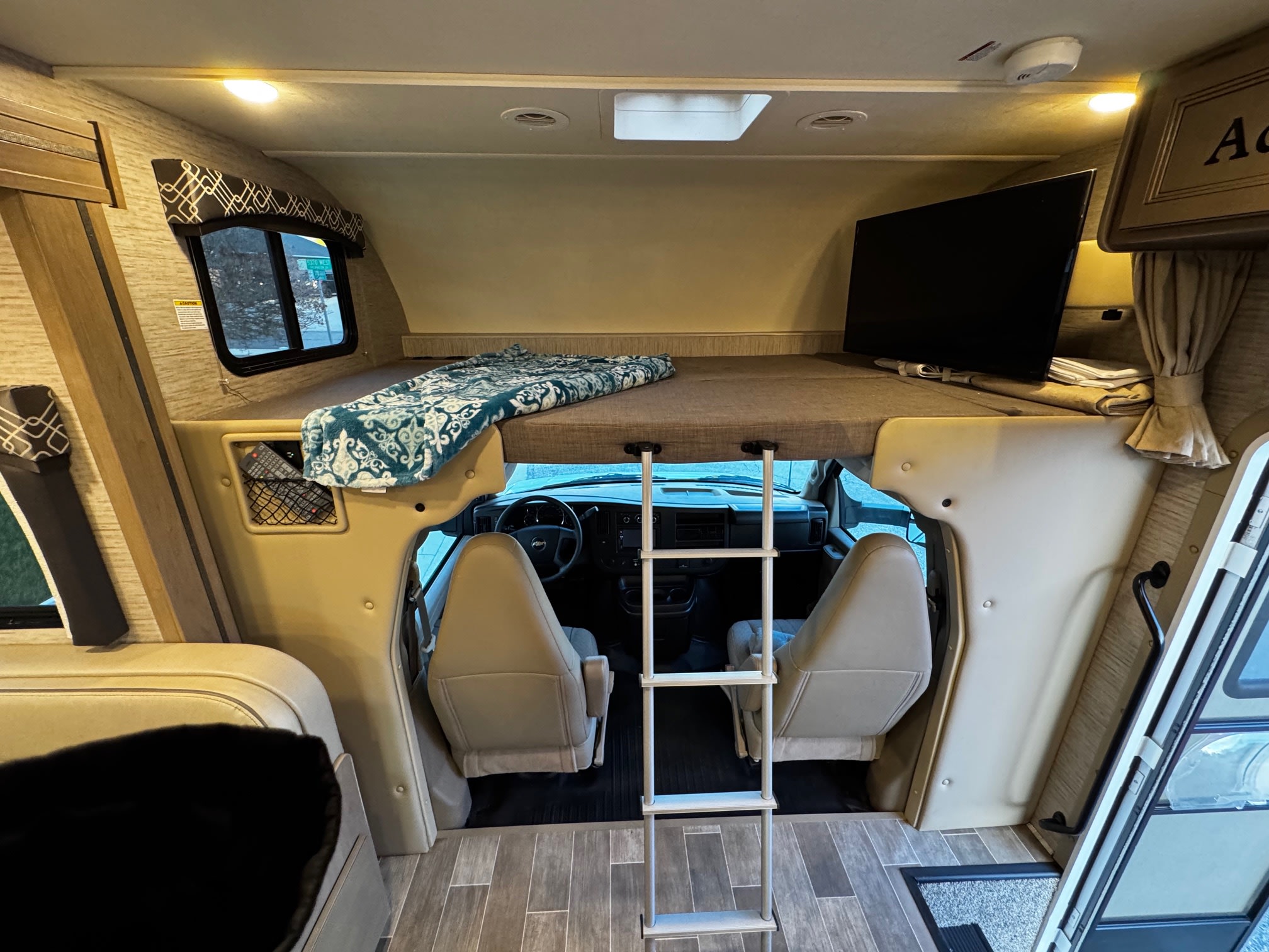 RV rental interior featuring a cab-over bunk bed with a ladder for access, a mounted TV, and the front driver/passenger cabin.. Thor Motor Coach Chateau 2021