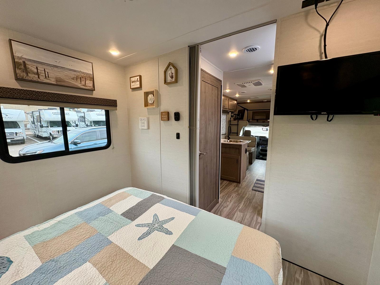 RV rental interior: a cozy, beach-themed bedroom connects to a functional living space with kitchen area. Ideal for travel.. Gulf Stream Conquest 2025