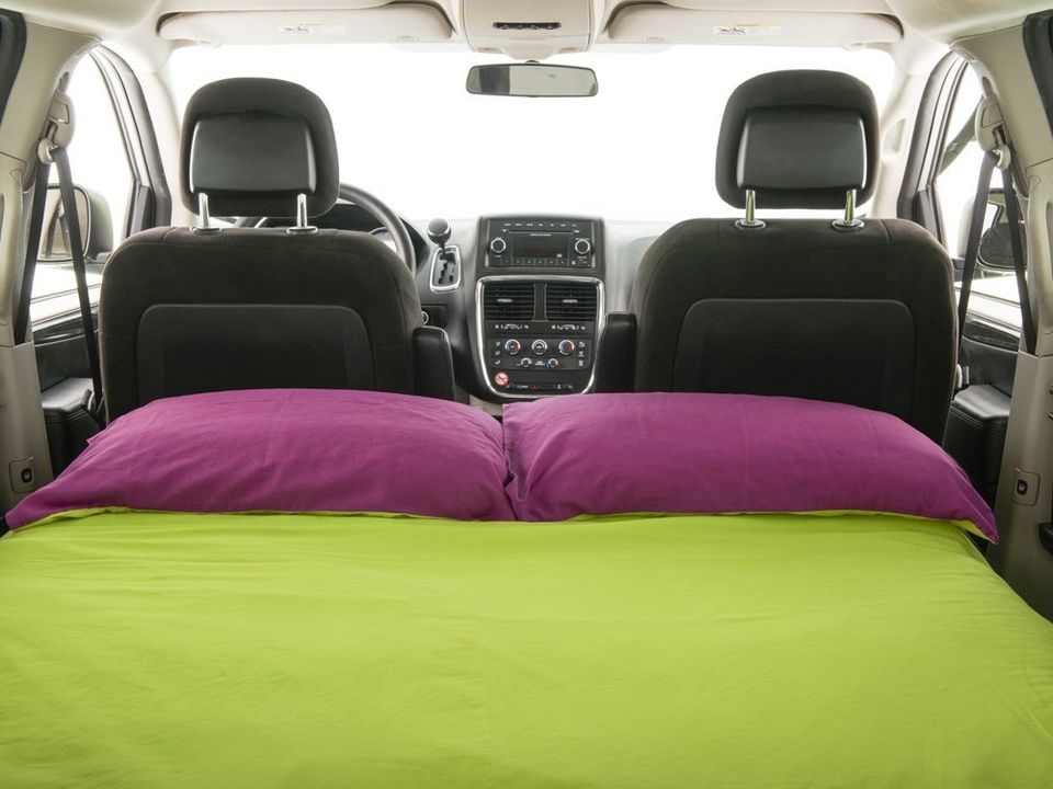 Inside this rv rental, a comfy bed with green sheets and purple pillows is set up in the van's rear for road trips & camping.. Dodge Grand Caravan 2012