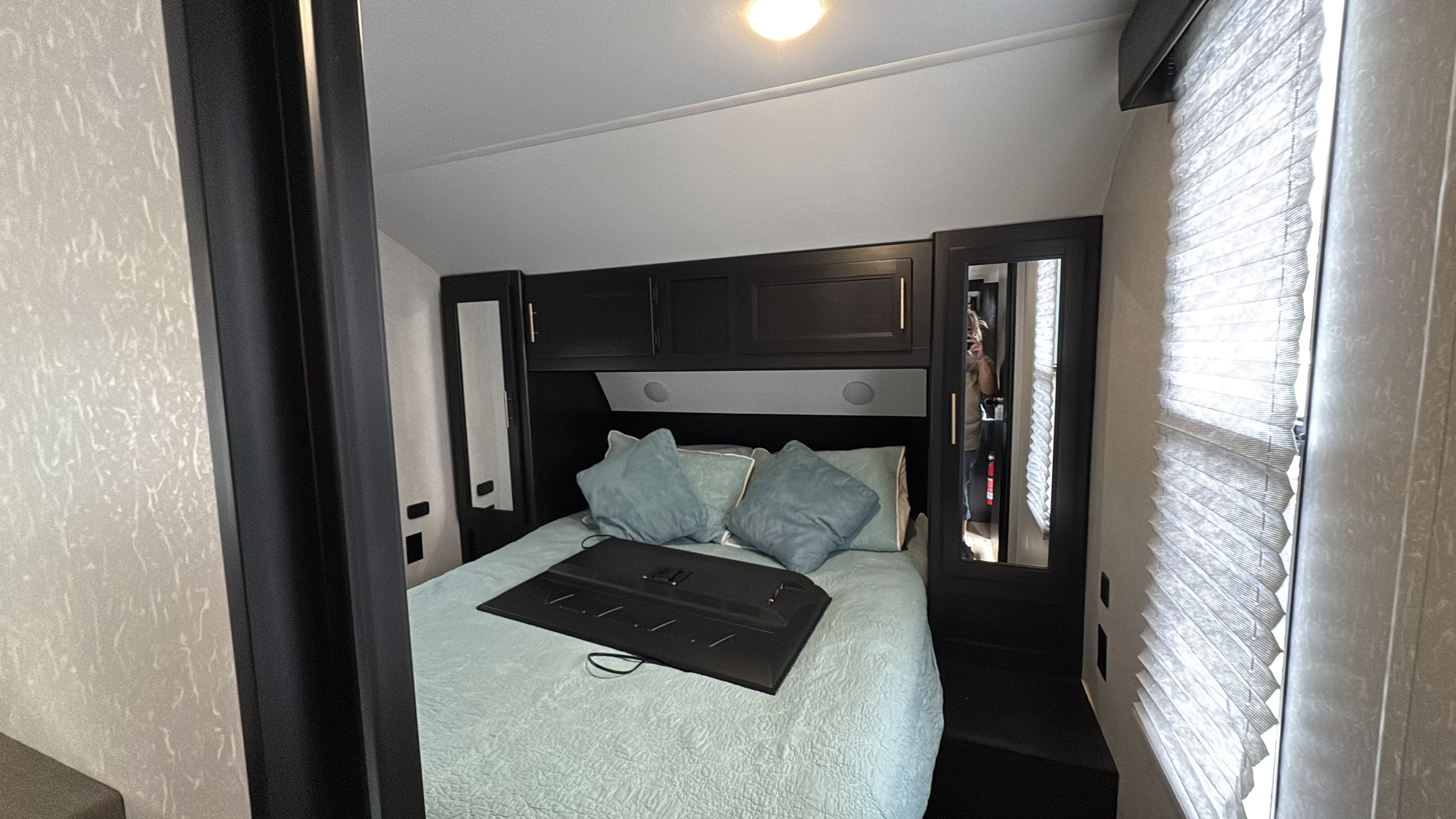 Cozy RV rental bedroom featuring a queen bed, dark overhead storage, mirrored closets, and a bright window with blinds.. Forest River Cherokee 2021