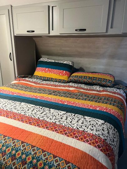 Cozy RV rental bedroom featuring a colorful striped quilt and overhead storage for travel.. Forest River Vibe 2022