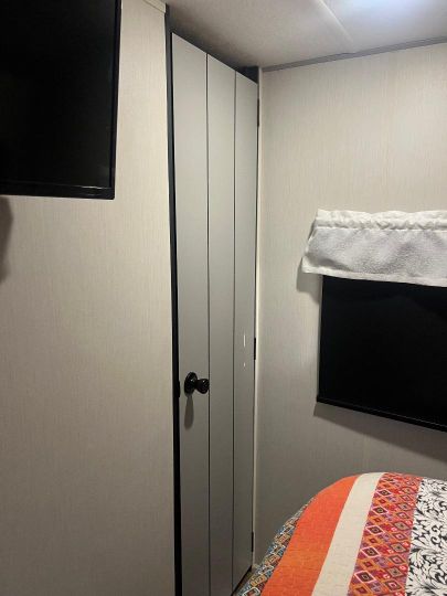 Compact RV rental bedroom with wall-mounted TVs, a narrow closet, and a colorful bed quilt, offering a cozy space.. Forest River Vibe 2022