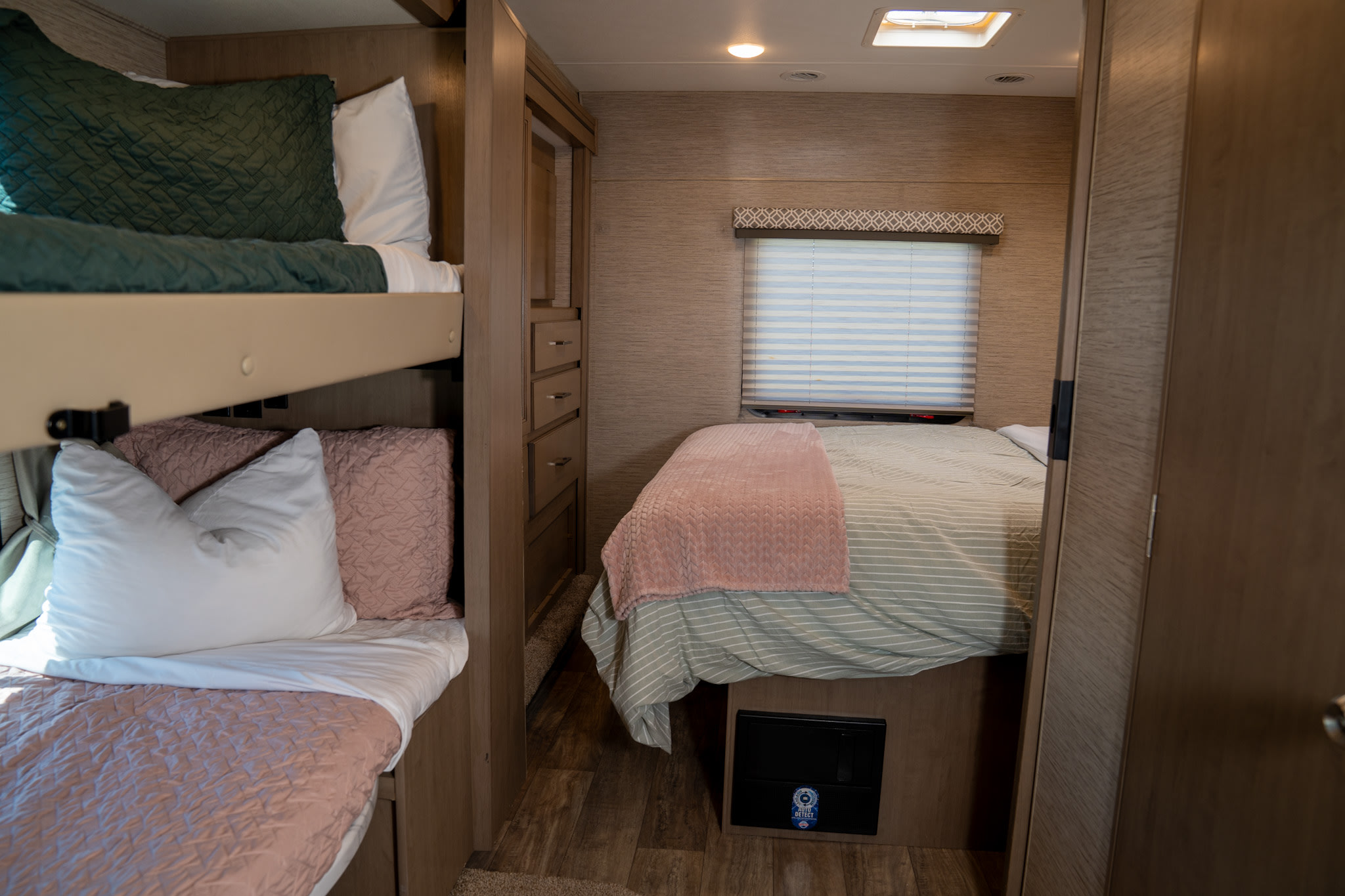 Cozy RV rental bedroom featuring comfortable bunk beds (green and pink) on the left and a striped main bed on the right.. Thor Motor Coach Coleman 2023