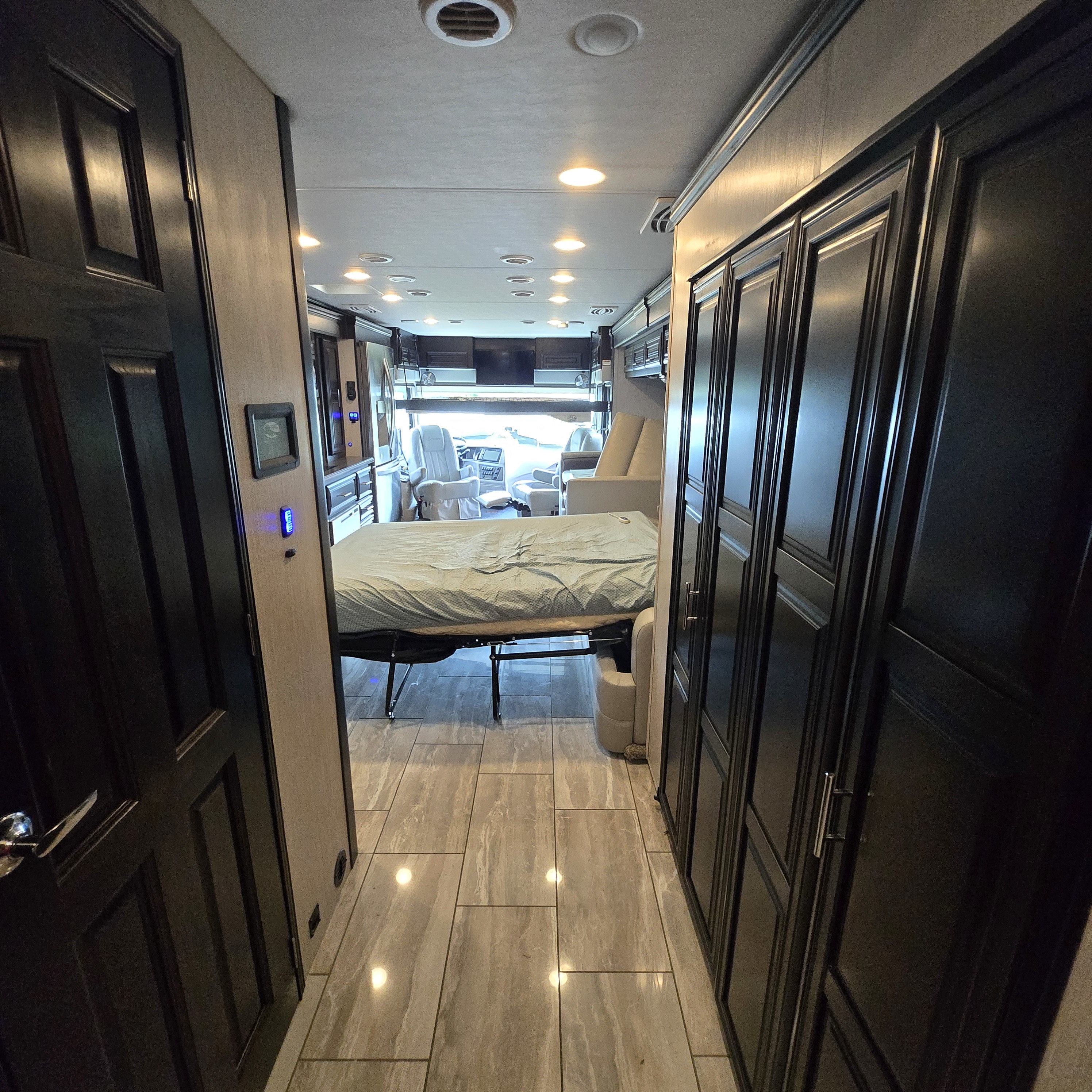 Explore a comfortable RV rental interior: a long hallway leads past dark wood cabinetry to a bed and the front cockpit. Modern flooring.. Berkshire XL 2022
