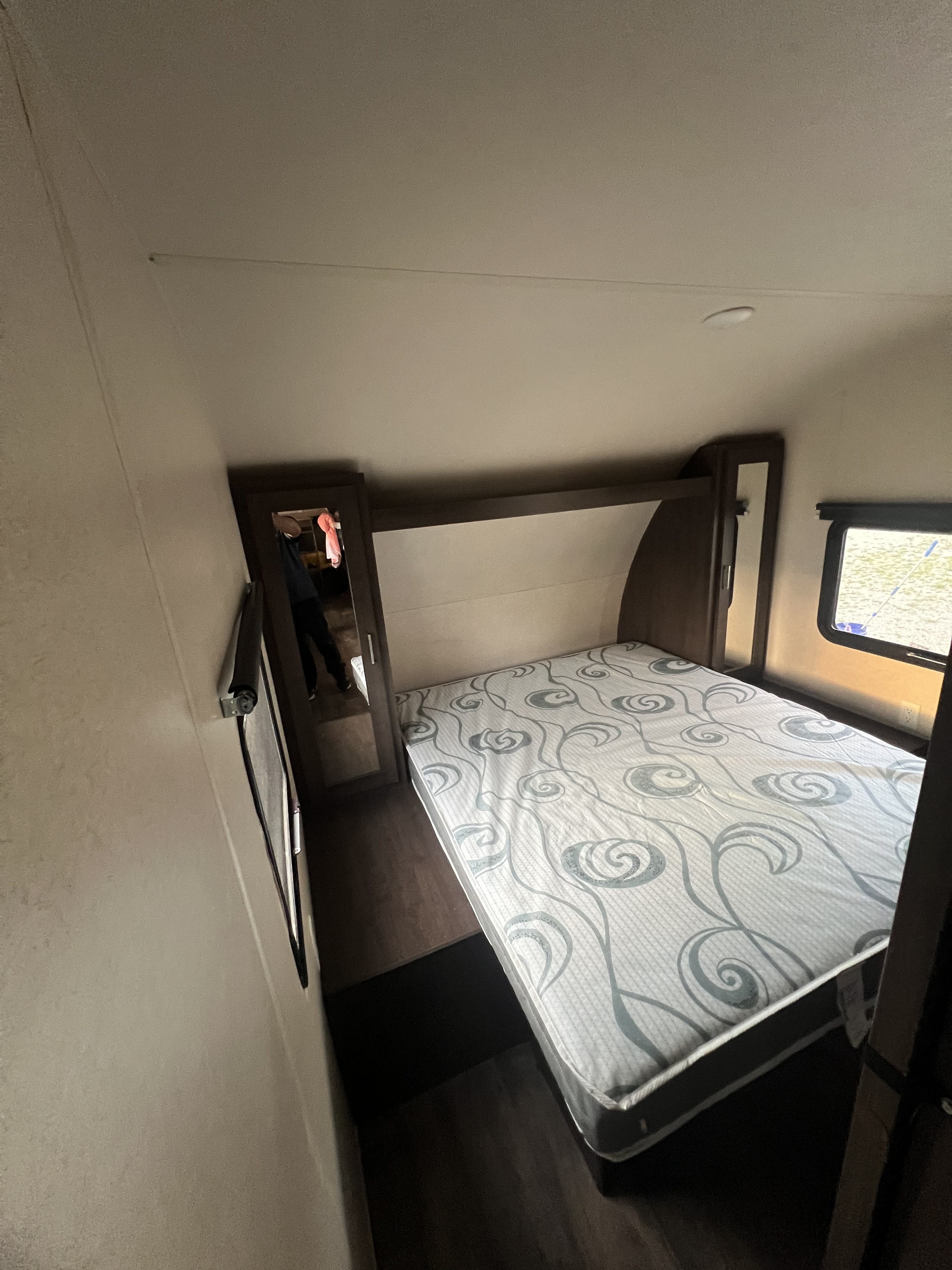 Well-designed RV rental bedroom: features a patterned bed, dark wood storage, mirror, and window. Perfect for your trip.. FOREST RIVER Wildwood X-Lite 2018