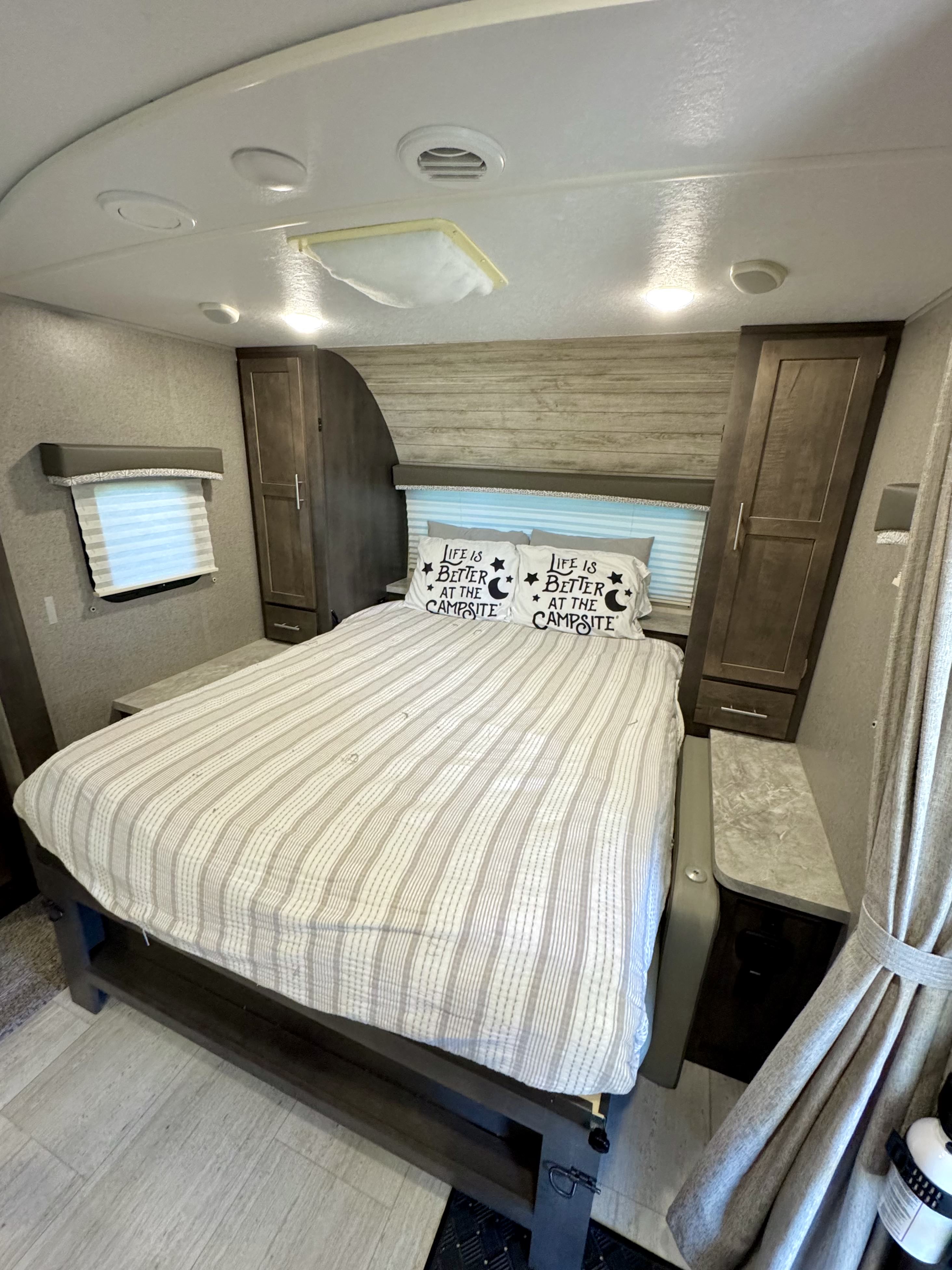 An inviting RV rental bedroom with a striped bed and "Life is better at the campsite" pillows, complete with storage and a window.. Forest River Rockwood Mini Lite 2019