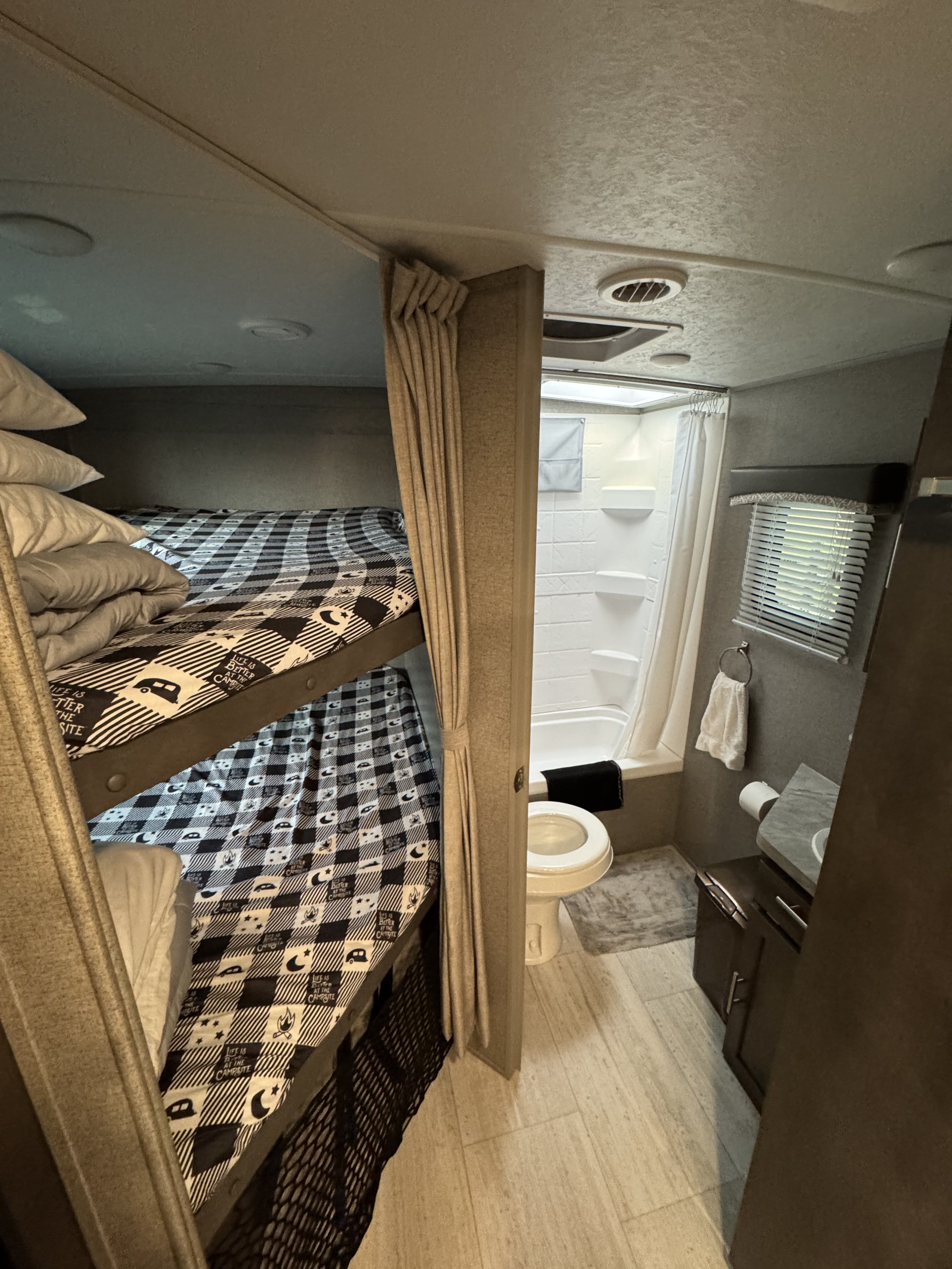 RV rental interior featuring cozy bunk beds with checkered bedding and a functional bathroom with a toilet and shower.. Forest River Rockwood Mini Lite 2019