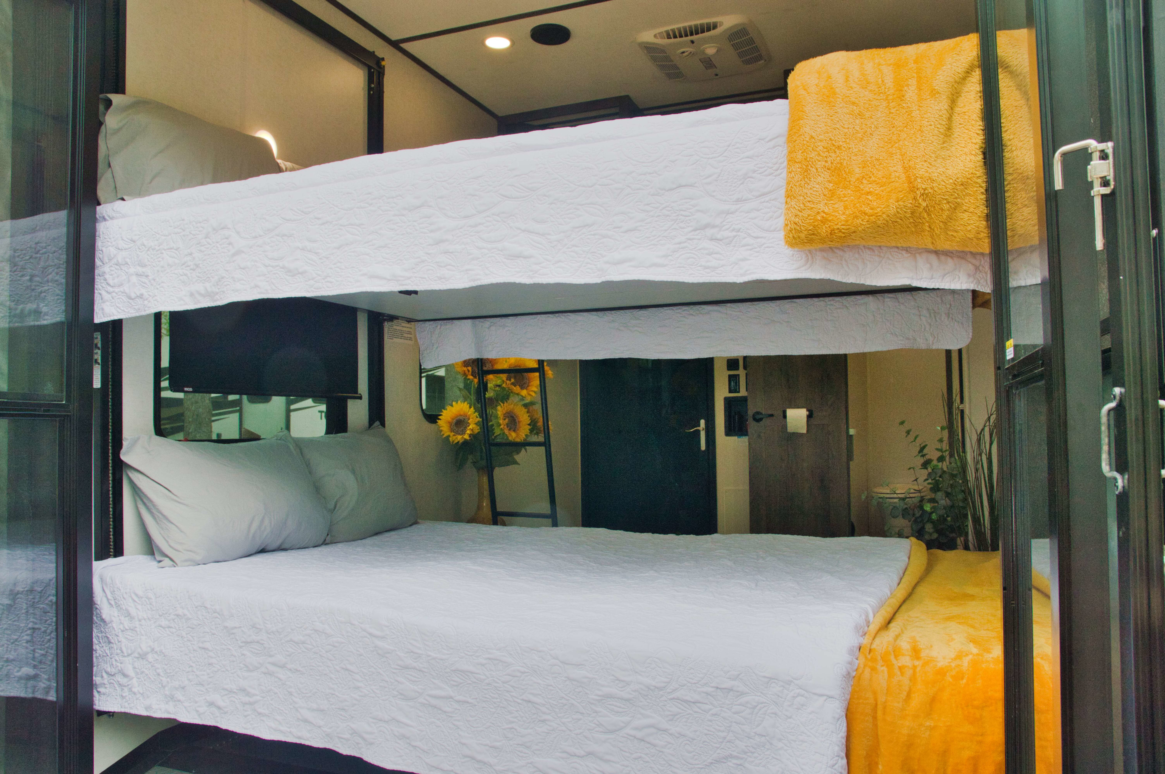 Explore this comfortable rv rental interior featuring bunk beds with fresh white bedding, grey pillows, and a cheerful yellow blanket.. Alliance Valor 2022