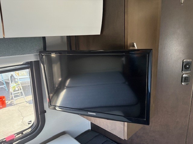 An RV rental's cozy interior, featuring a mounted TV, overhead storage, and a window view of the outside.. Leisure Travel Unity 2018