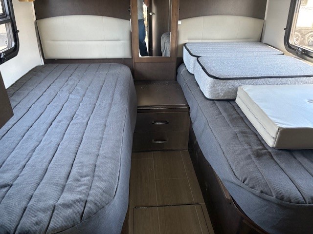 Compact RV rental bedroom featuring two twin beds, one with extra mattresses, separated by a nightstand.. Leisure Travel Unity 2018