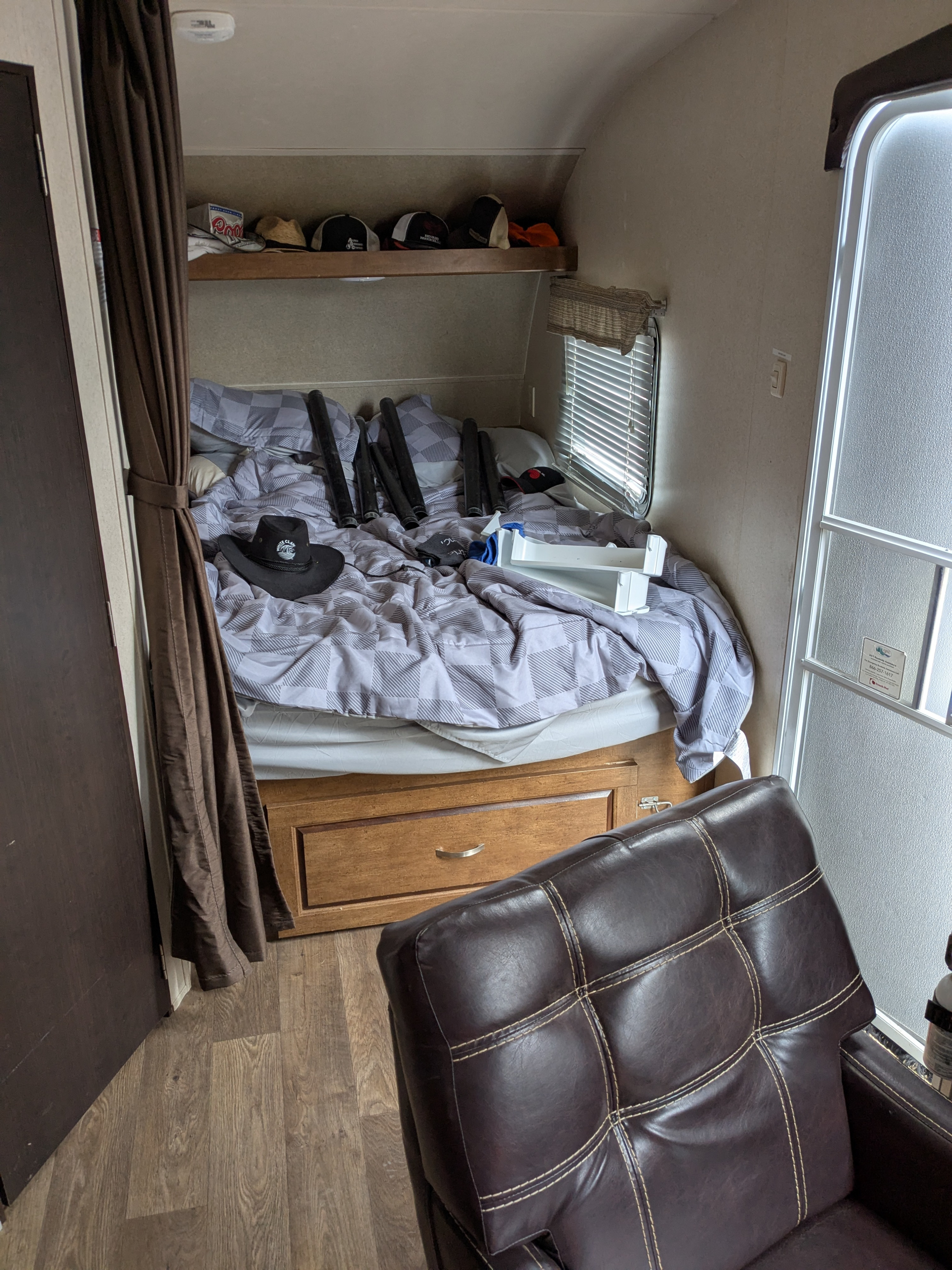 RV rental interior: A compact bedroom features a made bed with a hat & pipes, a shelf of hats, and a prominent leather chair.. Forest River Wildwood X-Lite 2018