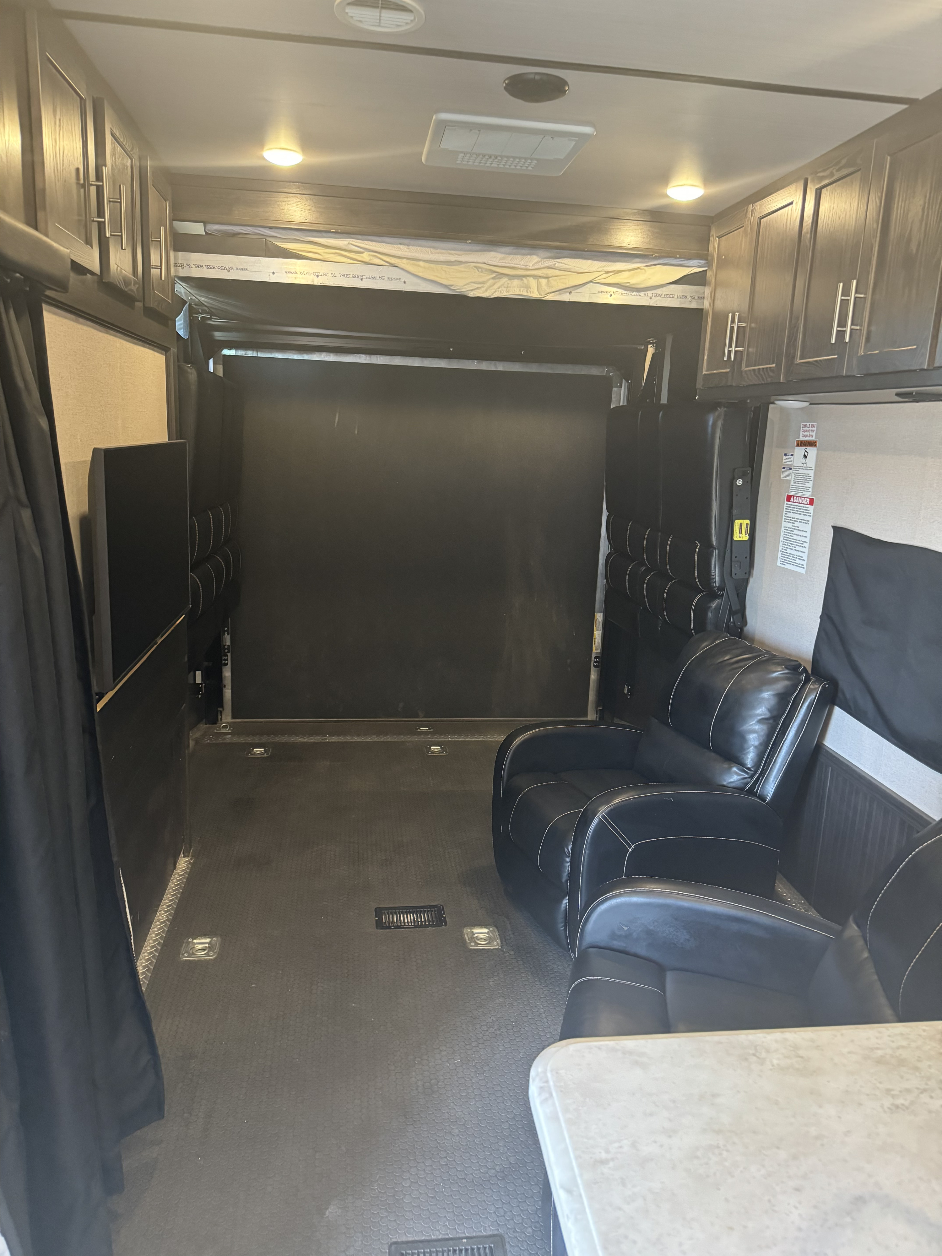 Inside an RV rental toy hauler, featuring a spacious cargo area, recliners, fold-up seating, and a bunk bed.. Forest River Nitro Xlr 2017