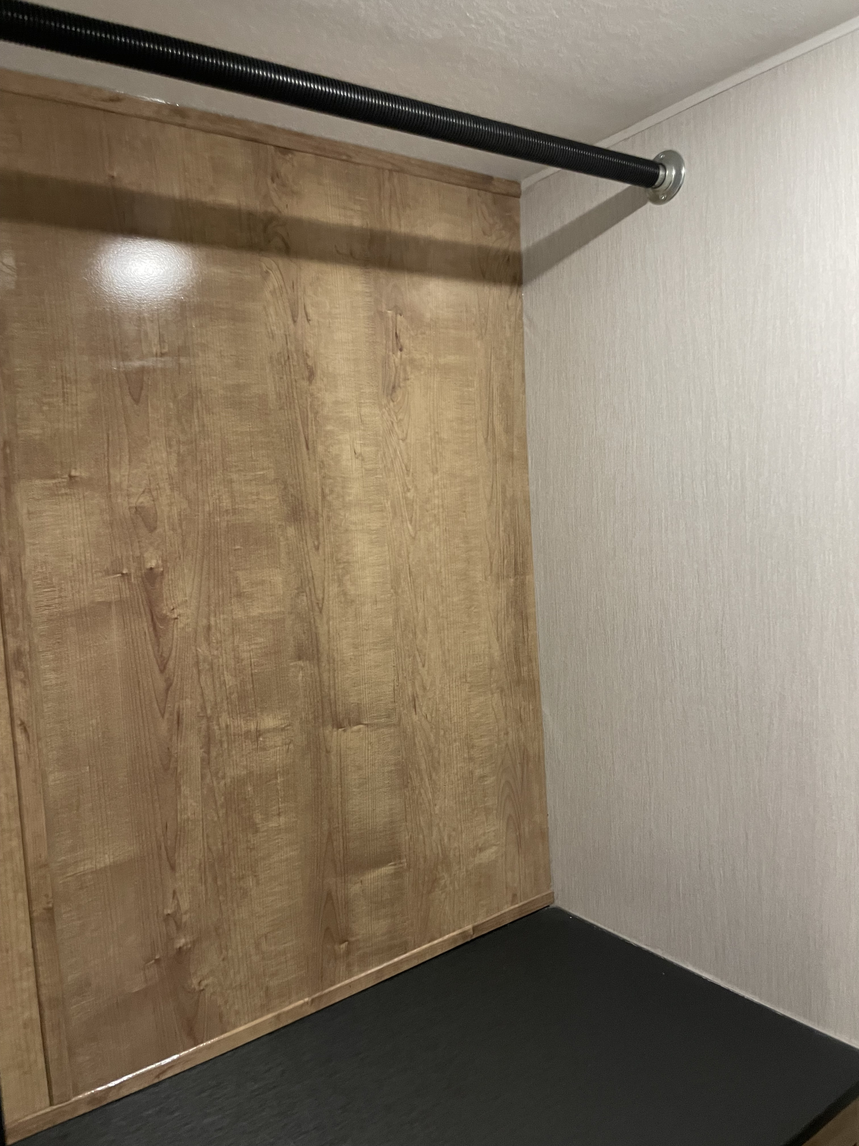 Compact *RV rental* closet featuring a wood-look wall, textured light wall, and black hanging rod for clothes.. Forest River Coachmen Leprechaun 2020