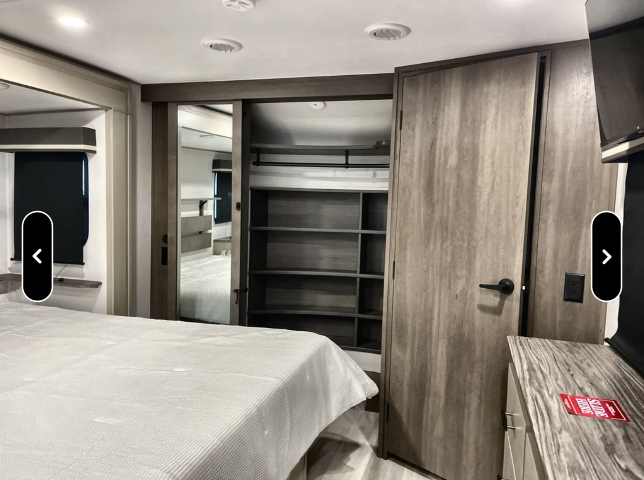 Modern RV rental bedroom interior with a bed, mirrored sliding closet doors, and ample storage shelves.. Grand Design Influence 2024
