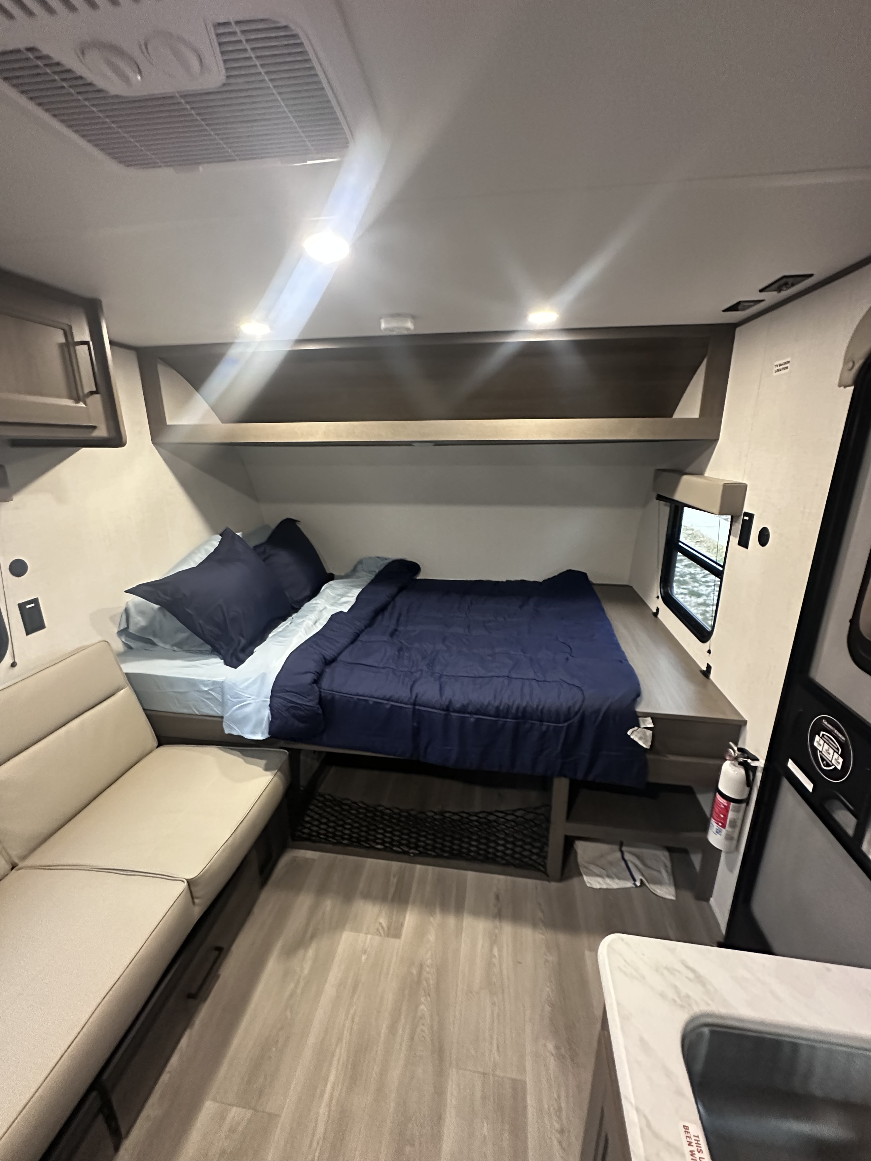 Cozy RV rental interior showcasing a bed with blue bedding, a tan sofa, and overhead storage.. grand design transcend one 2025