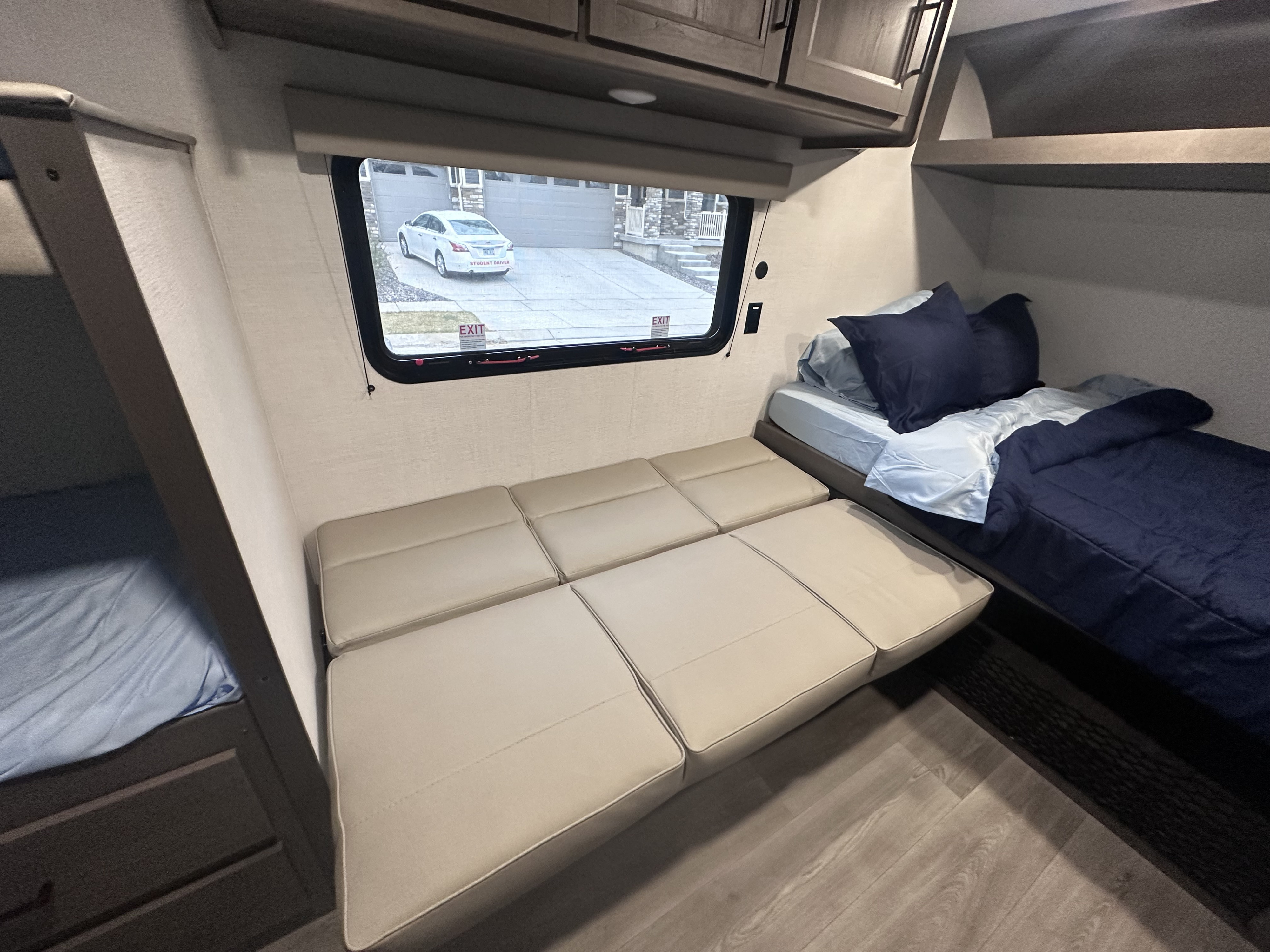 RV rental interior featuring bunk beds, convertible seating, and a window view showing a residential street with a car outside.. grand design transcend one 2025