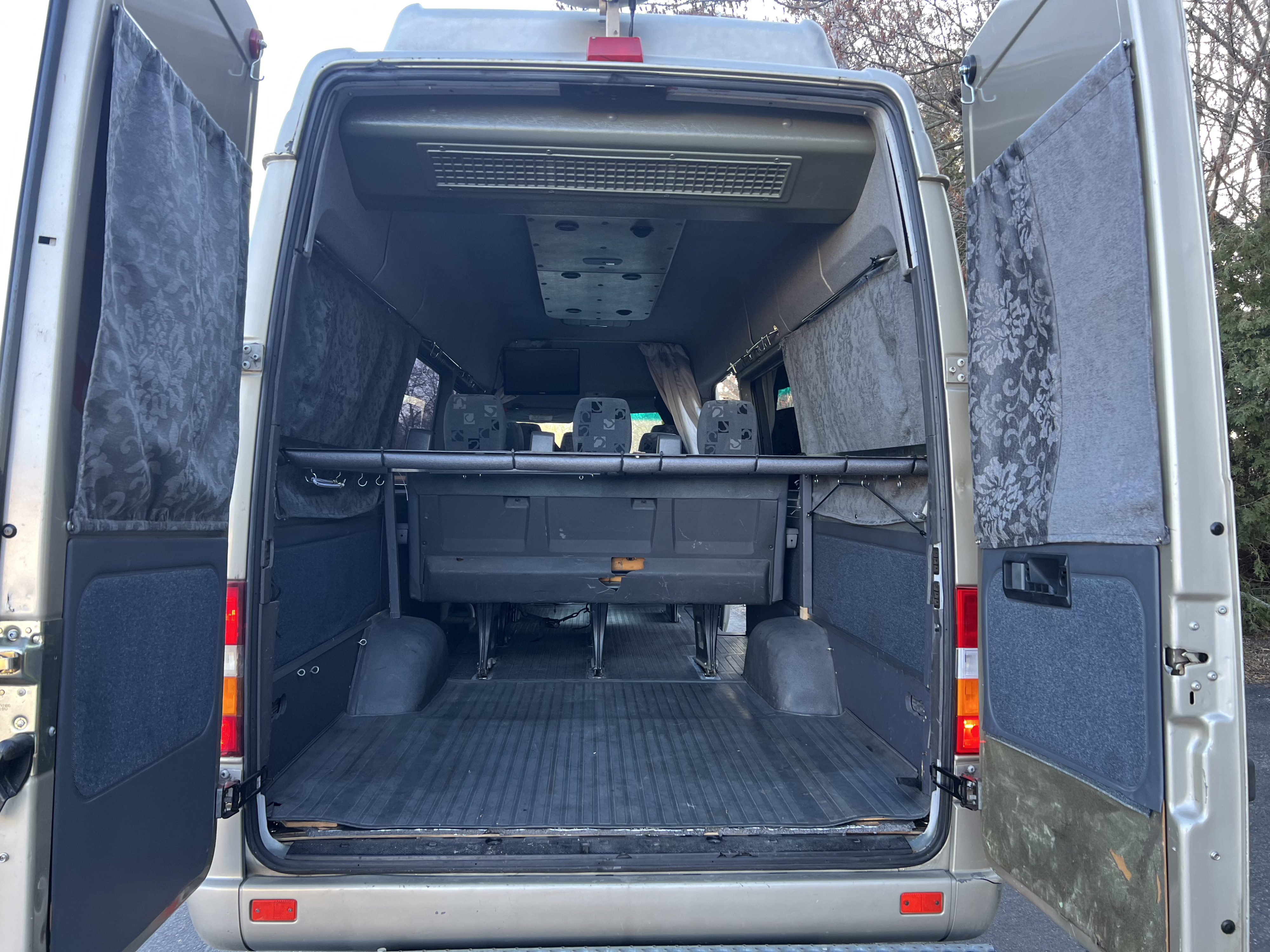 Rear view of an RV rental van's interior with open doors, showing passenger seats, ribbed floor, and overhead AC.. Mercedes Sprinter 2006
