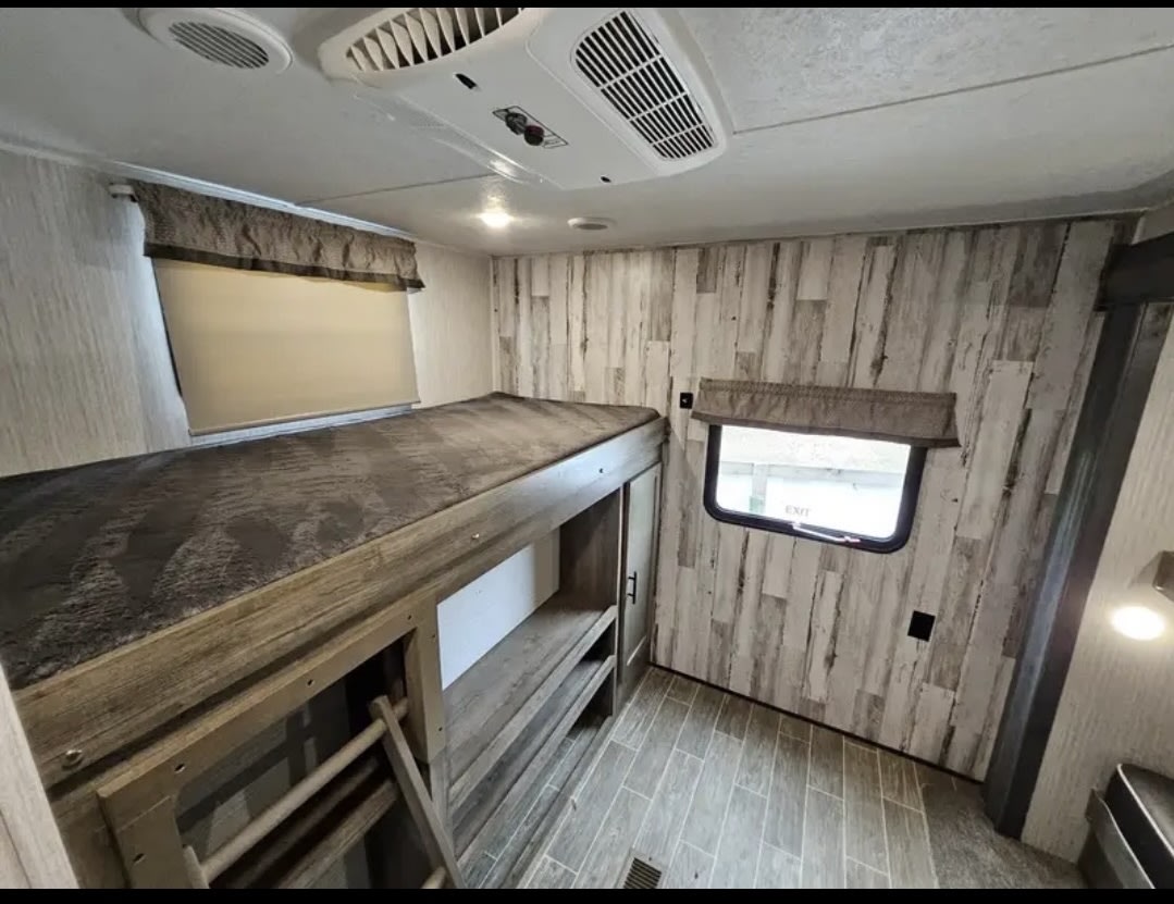 Spacious RV rental interior with bunk beds, wooden accents, and windows. Ideal for family sleeping in a travel trailer.. Forest River Puma 2020