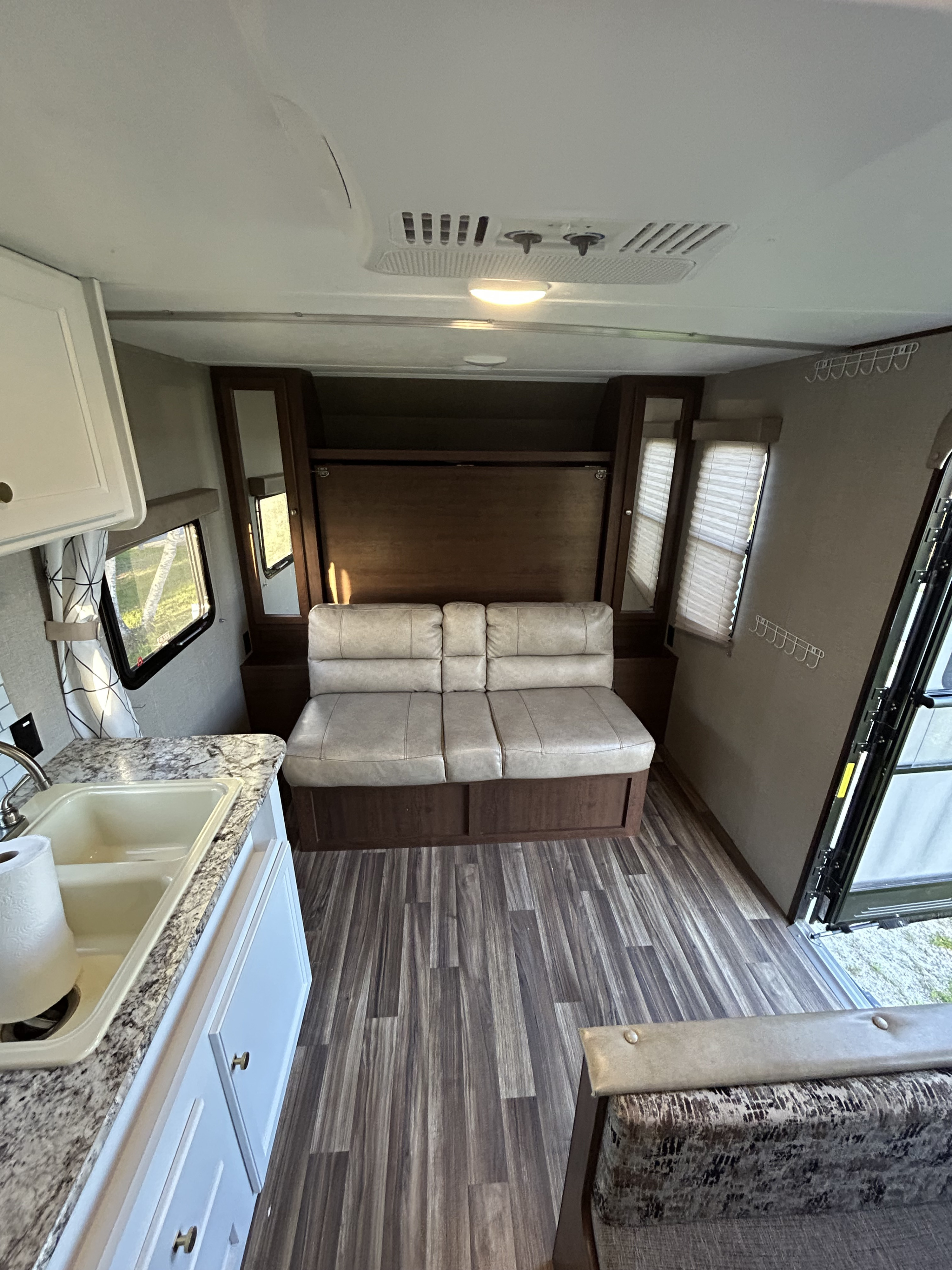 RV rental interior: kitchen with sink, comfy sofa, wall bed system, and wood-look flooring. Ready for your trip!. Keystone Hideout 2018