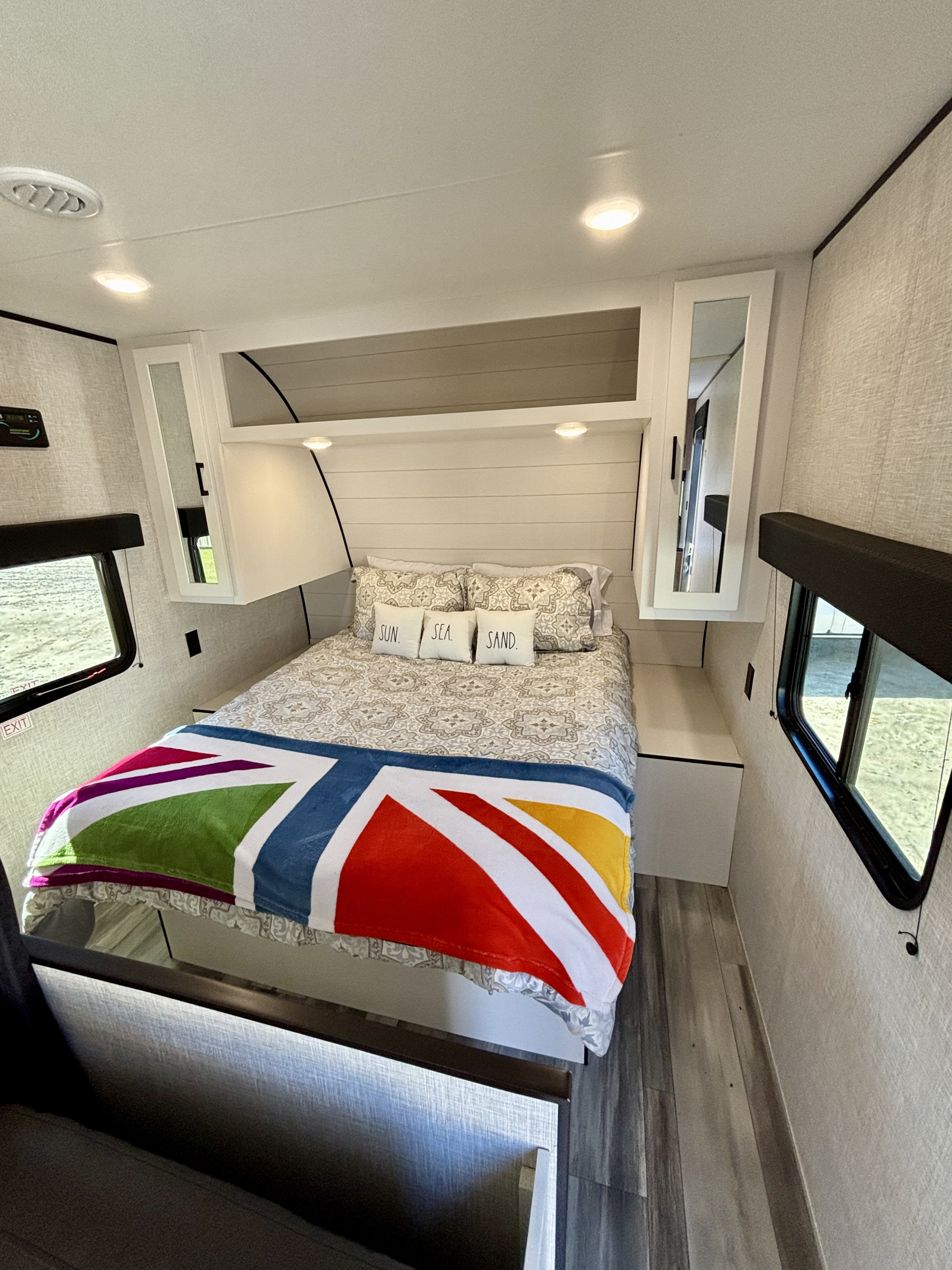 Cozy RV rental bedroom with 'Sun. Sea. Sand.' pillows, a vibrant blanket, and overhead storage.. Jayco Jay Flight SLX 2024