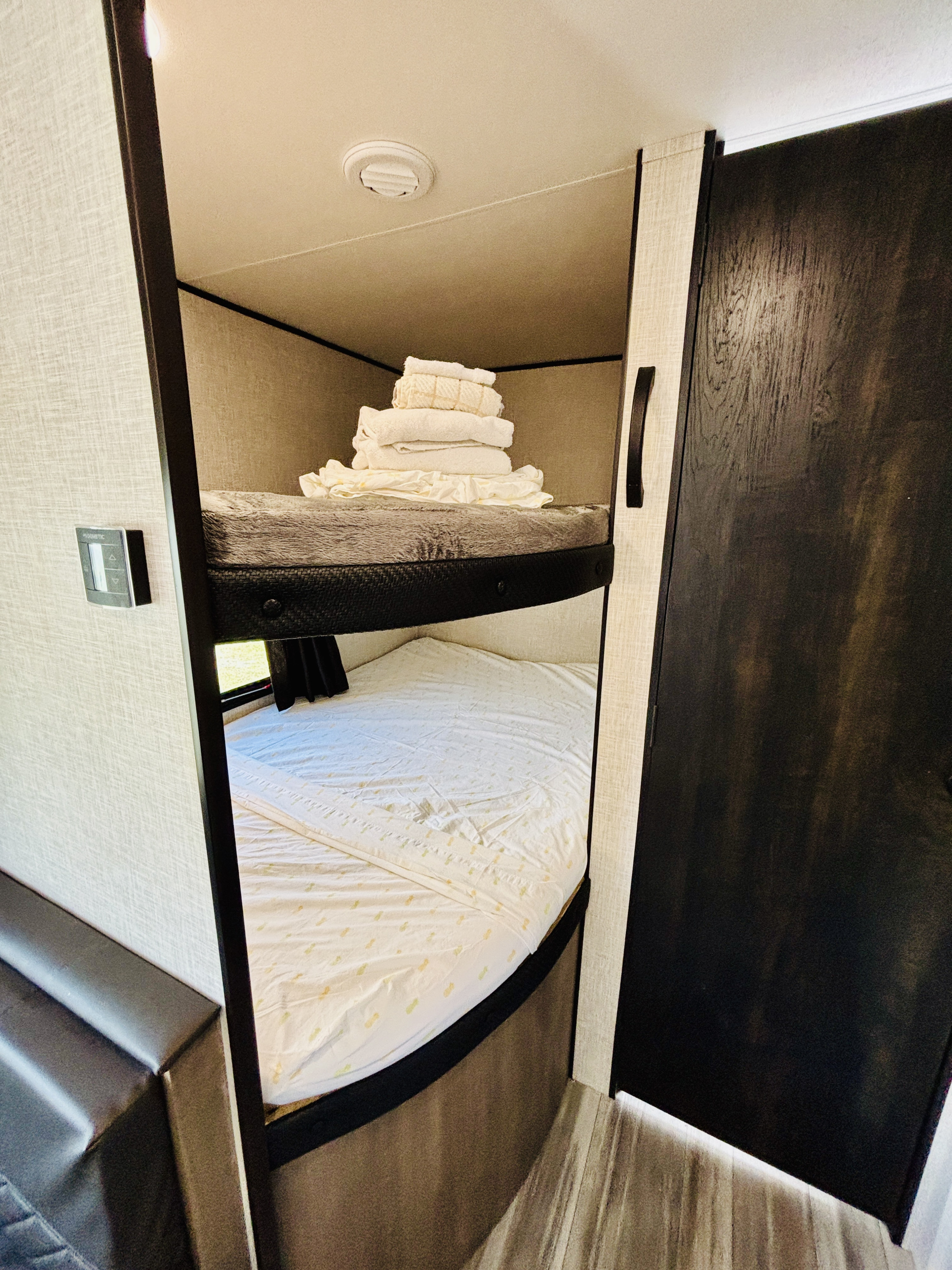 Clean, compact bunk beds in this cozy RV rental. The upper bunk holds neat towels; the lower, pineapple-patterned sheets await guests.. Jayco Jay Flight SLX 2024