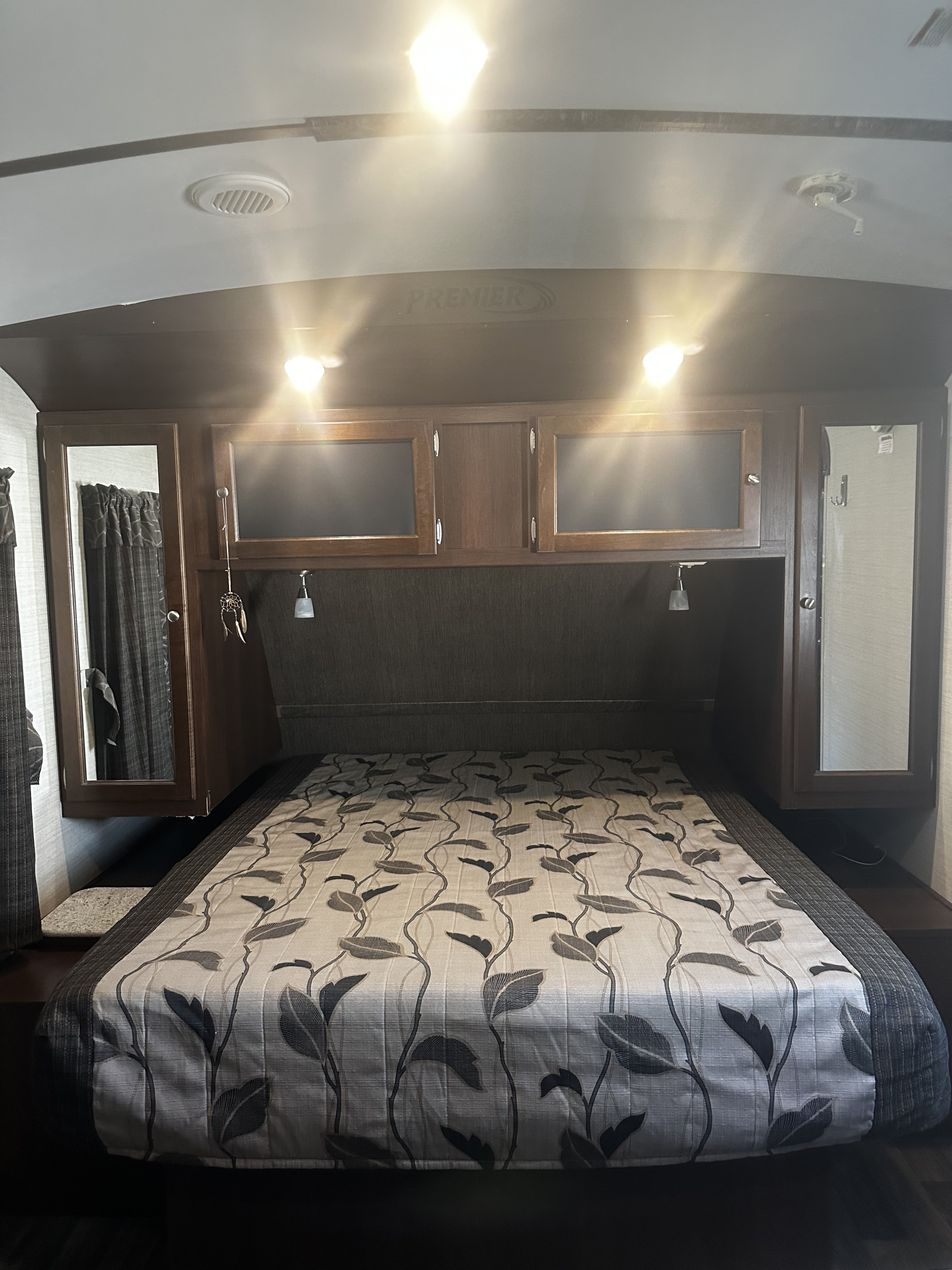 Cozy RV rental bedroom featuring a patterned bed, modern overhead cabinets, and reading lights for comfortable stays.. Keystone RV Bullet Premier 2016