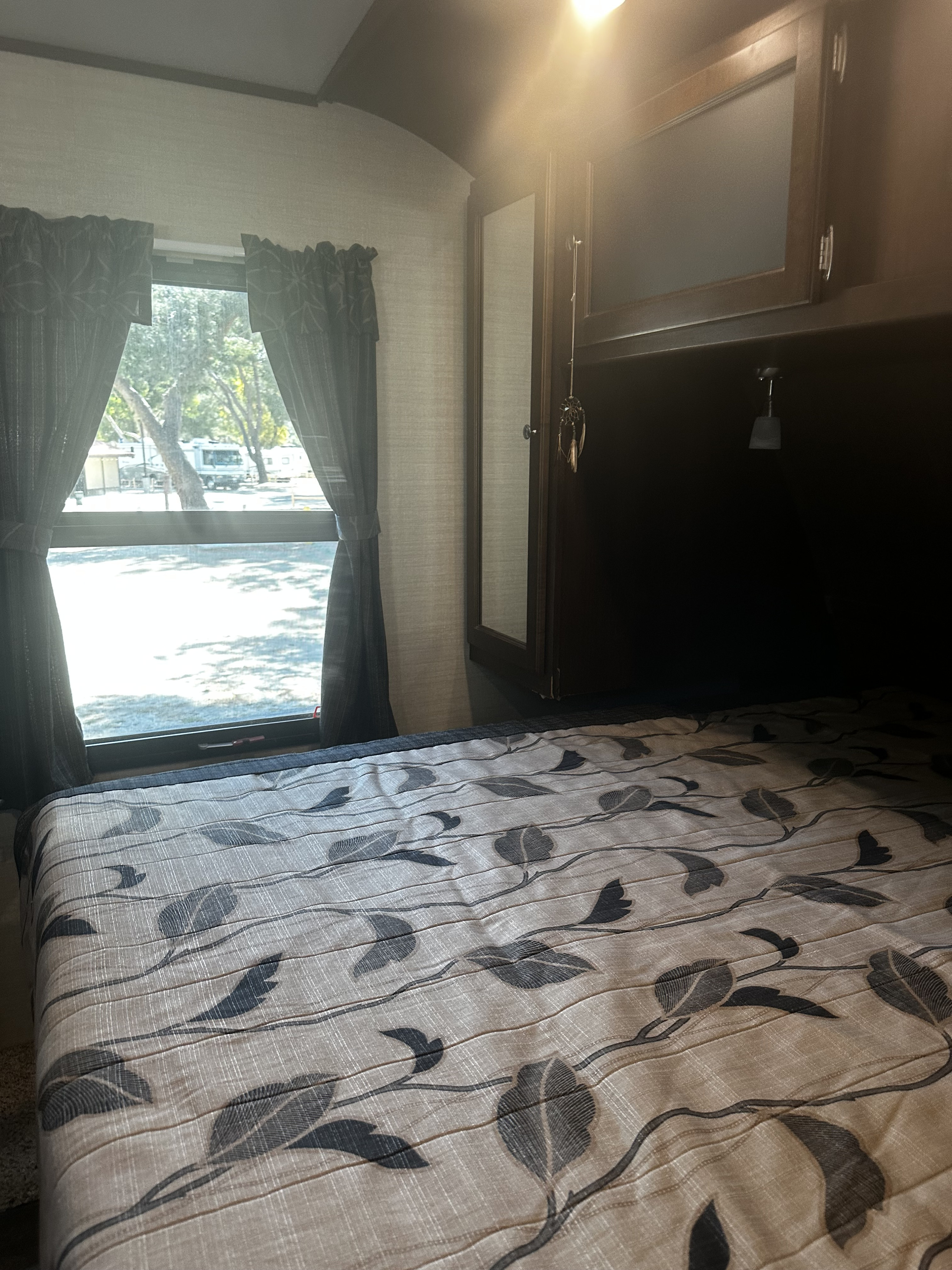 Inside an RV rental bedroom: patterned bed, window to a campground, and overhead storage.. Keystone RV Bullet Premier 2016