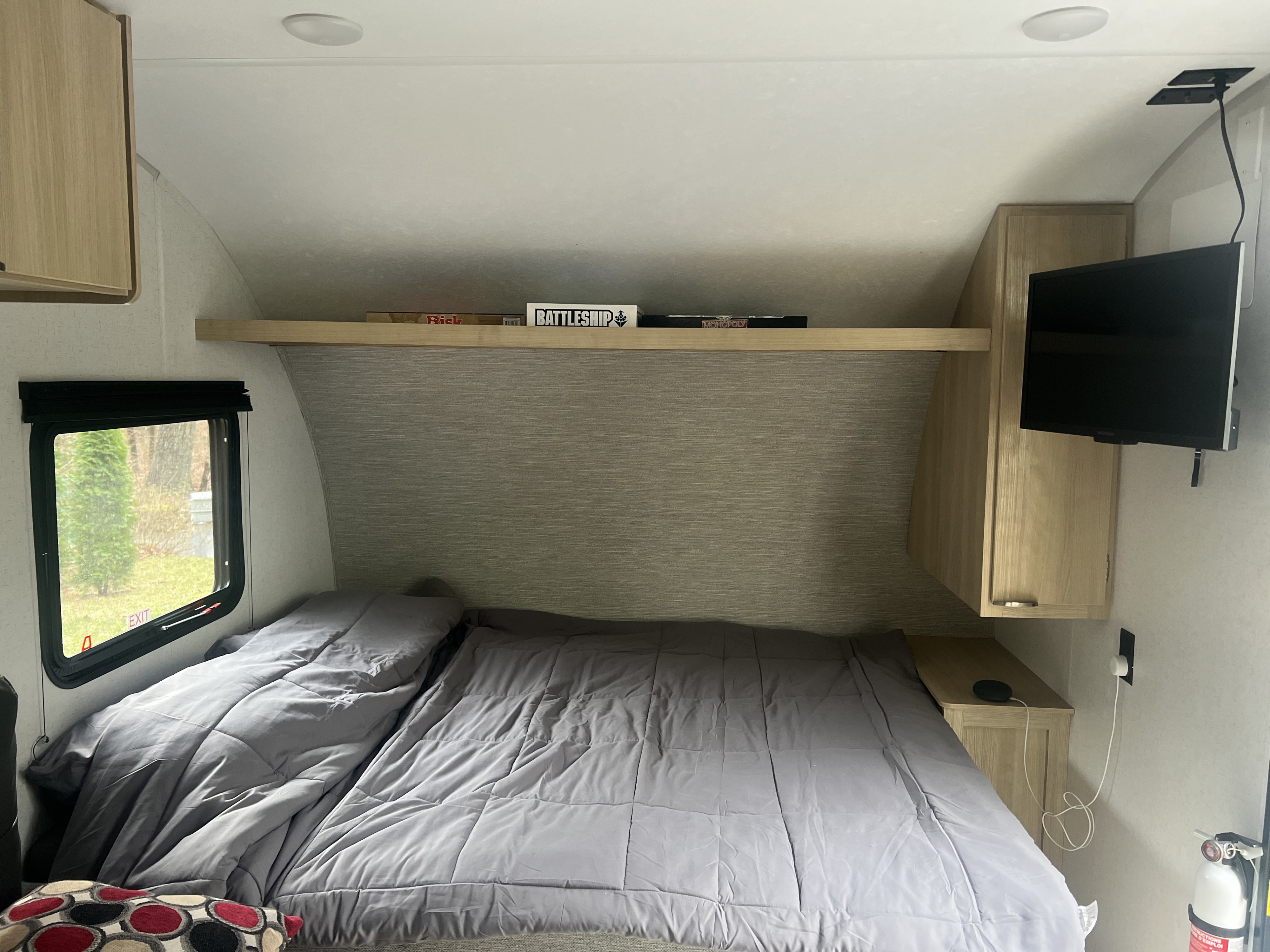 Cozy RV rental bedroom with grey bedding, overhead shelf holding board games (Battleship), and a wall-mounted TV.. Forest River Salem 2024