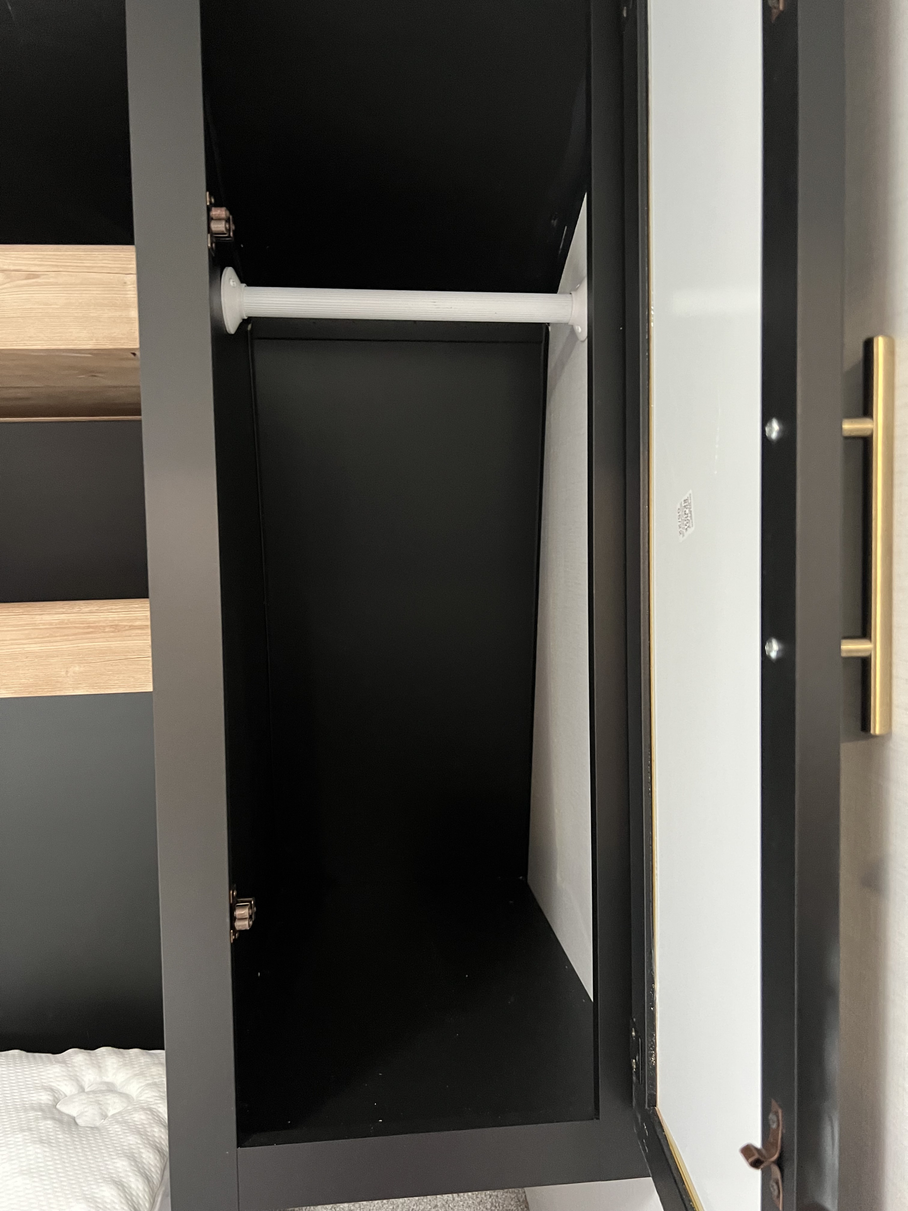 Inside a compact RV rental wardrobe: black interior, white hanging rod, and door with mirror.. Keystone RV Springdale 2022