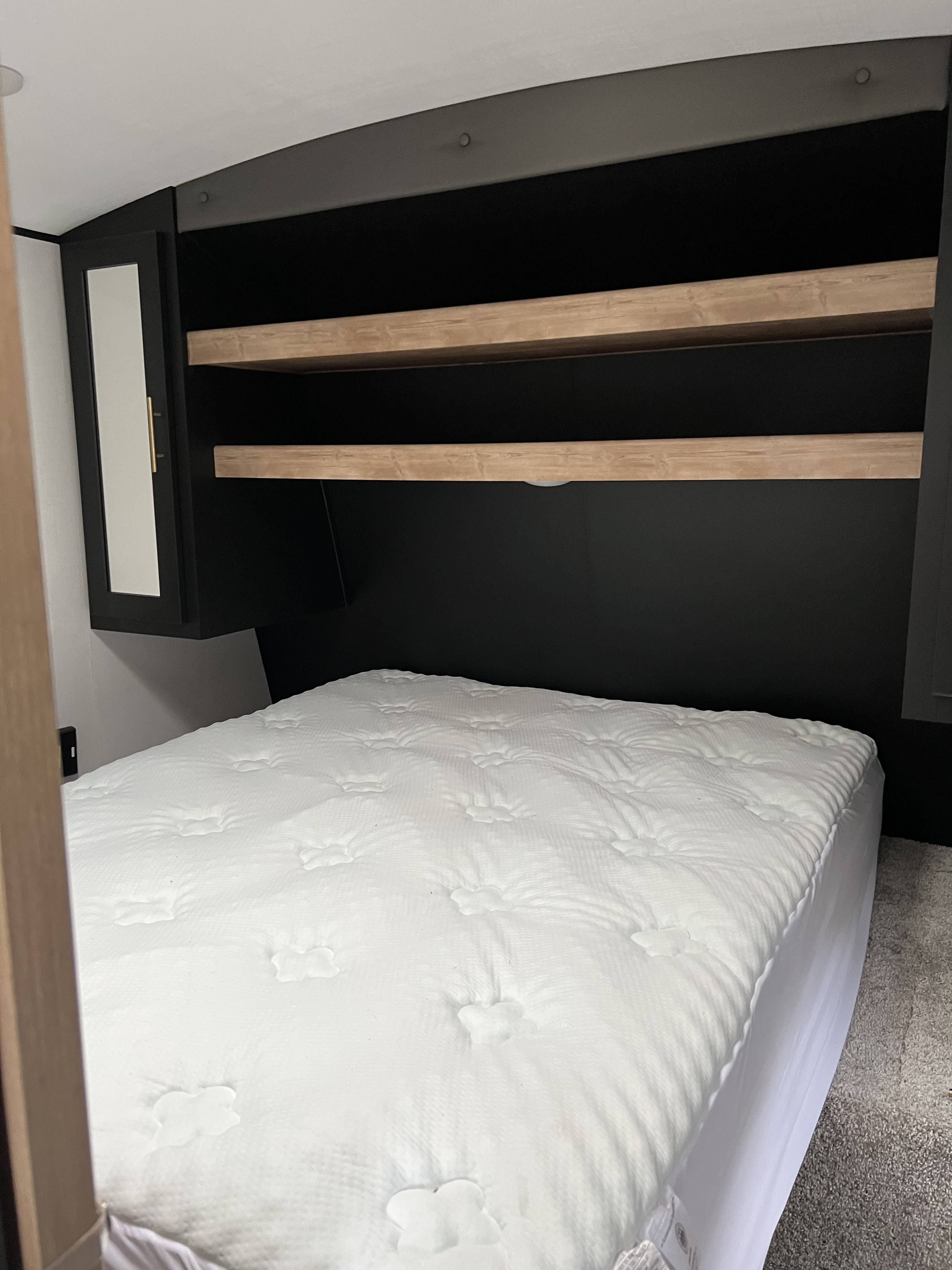 Cozy RV rental bedroom: clean white mattress, storage shelves, mirrored cabinet & lighting.. Keystone RV Springdale 2022