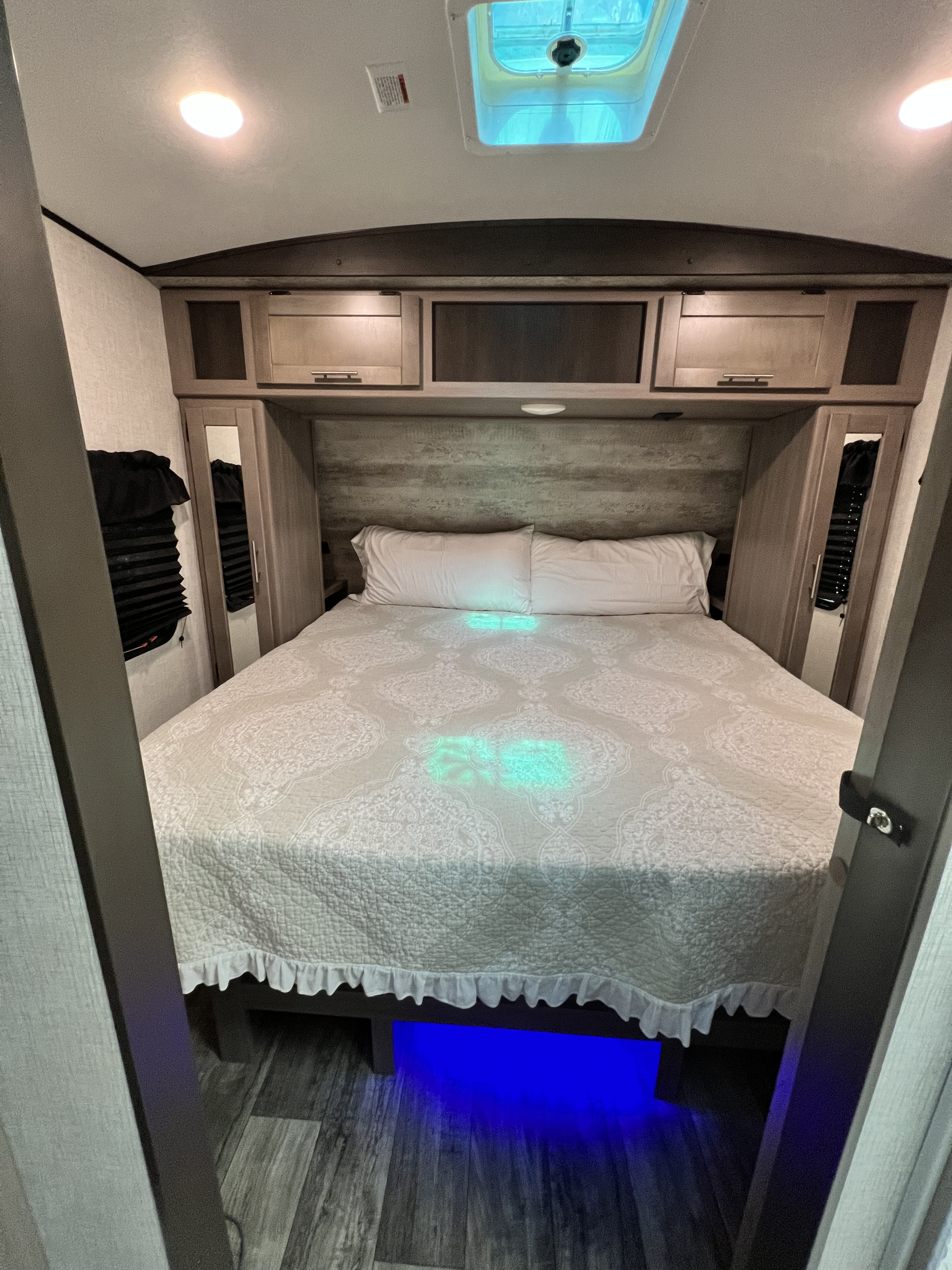 Cozy RV rental bedroom with modern overhead cabinets, bright lighting, and ambient blue under-bed glow for a comfortable stay.. Crossroads RV Sunset Trail Super Lite 2021