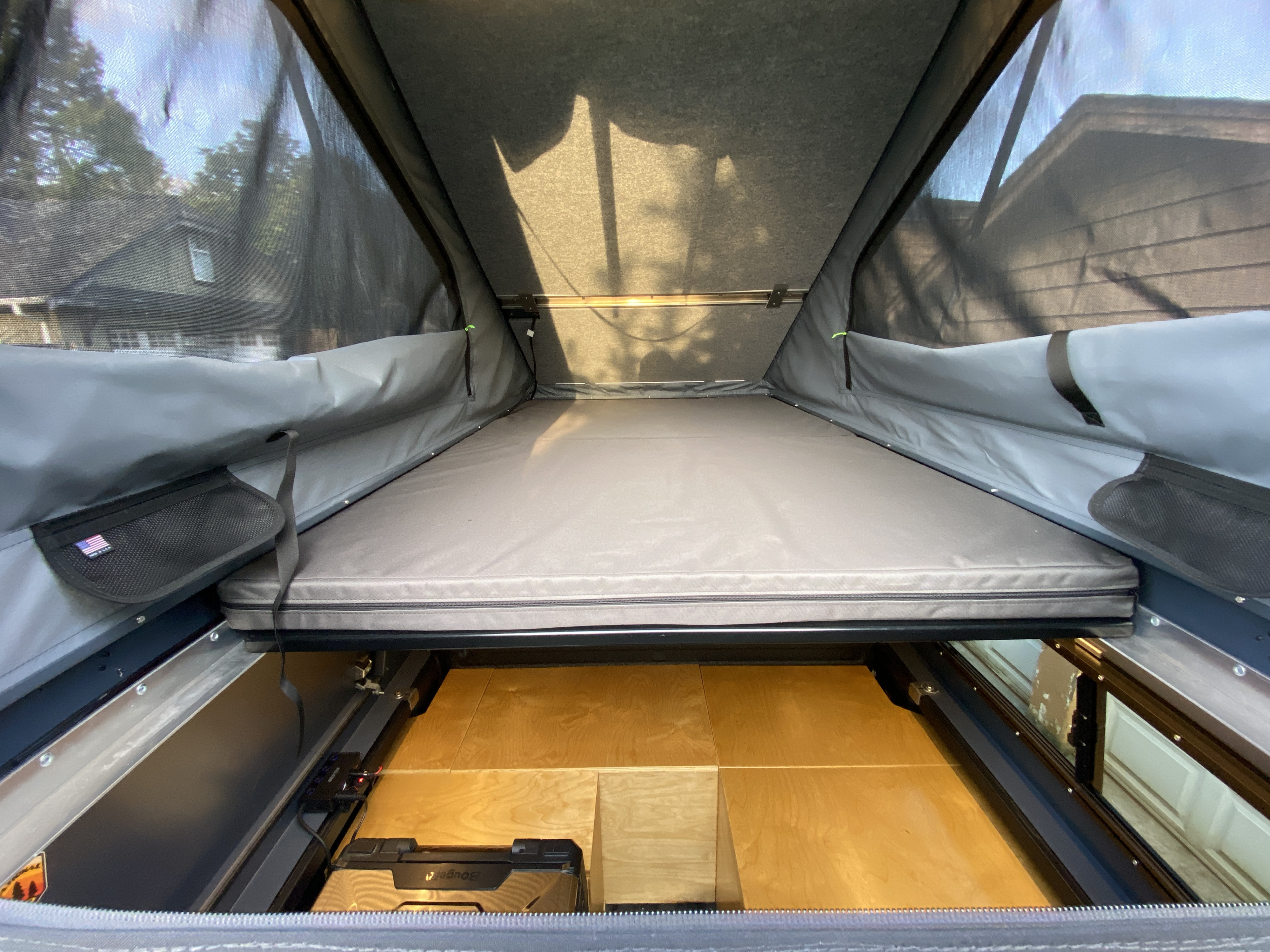 RV rental rooftop tent interior, showing a sleeping area, under-bed storage, and mesh windows with outdoor view.. Chevrolet Colorado 2024