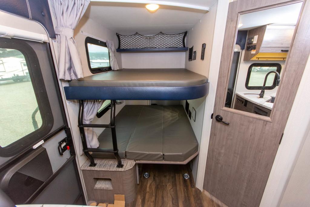 Inside an RV rental: space-saving bunk beds with ladder, windows, and a mirrored door reflecting the compact kitchen area.. Lance Manufacturing Lance Manufacturing Trailer 2021