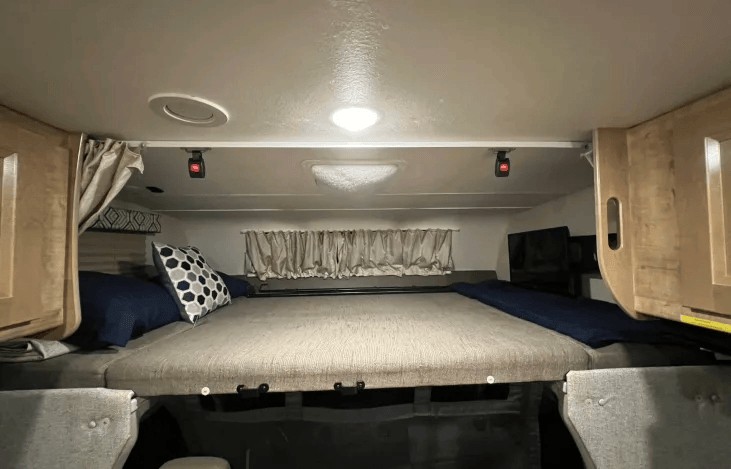 Cozy sleeping area in an RV rental, featuring a large bed, overhead lights, and storage cabinets for comfort.. Coachmen Leprechaun 260RS 2020