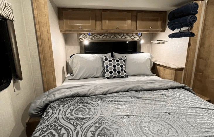 Inside this inviting RV rental, a comfortable bedroom features a bed, overhead storage, and convenient towel rack.. Coachmen Leprechaun 260RS 2020