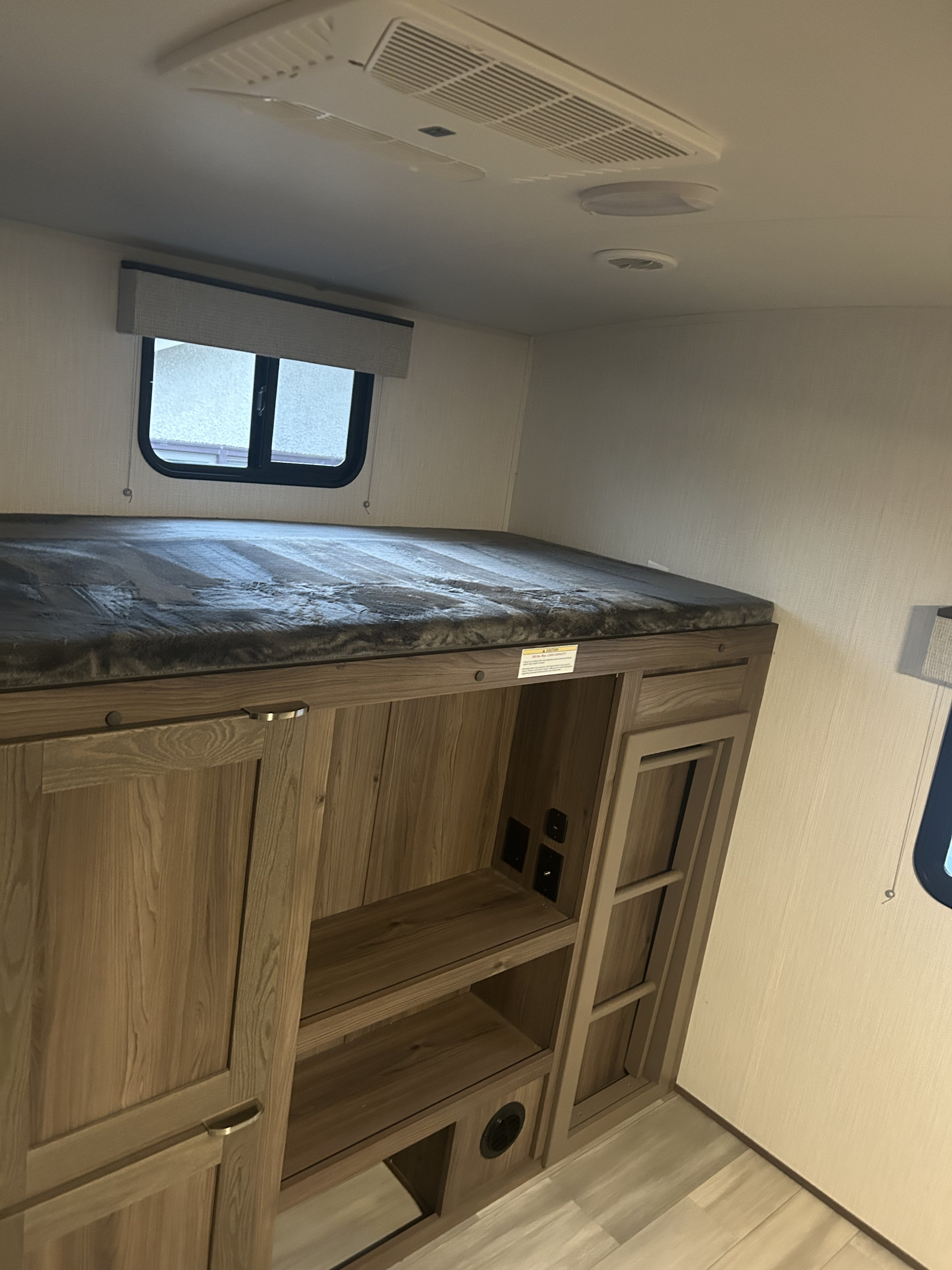 Cozy RV rental interior showcasing a bunk bed with a window, AC unit, and integrated wooden storage and outlets.. MPG 3100BH 2025