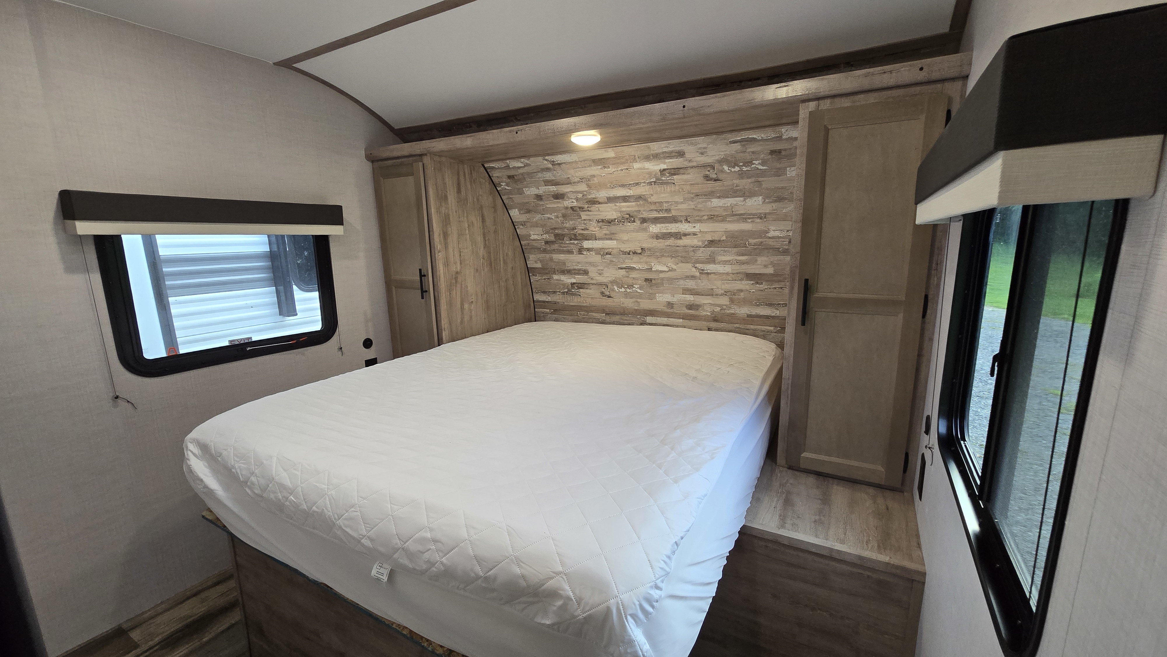 Spacious RV rental bedroom with a comfy bed, modern headboard, built-in storage closets, and windows for natural light.. Gulf Stream Trailmaster 2024