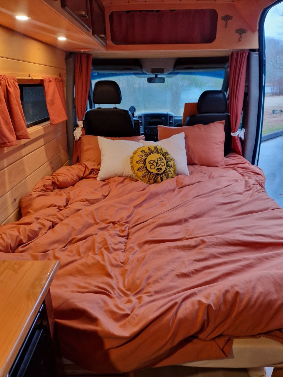 Step into comfort! This RV rental features a large bed with warm orange bedding & a sun pillow, set in a wood-paneled interior.. Dodge Sprinter Van 2008