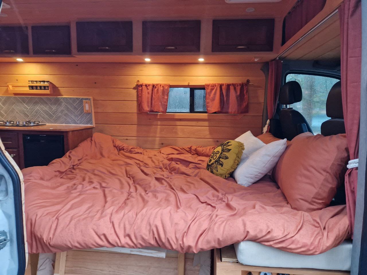 Cozy RV rental interior with a large bed, kitchen, and warm wood walls. Ideal for van life adventures.. Dodge Sprinter Van 2008